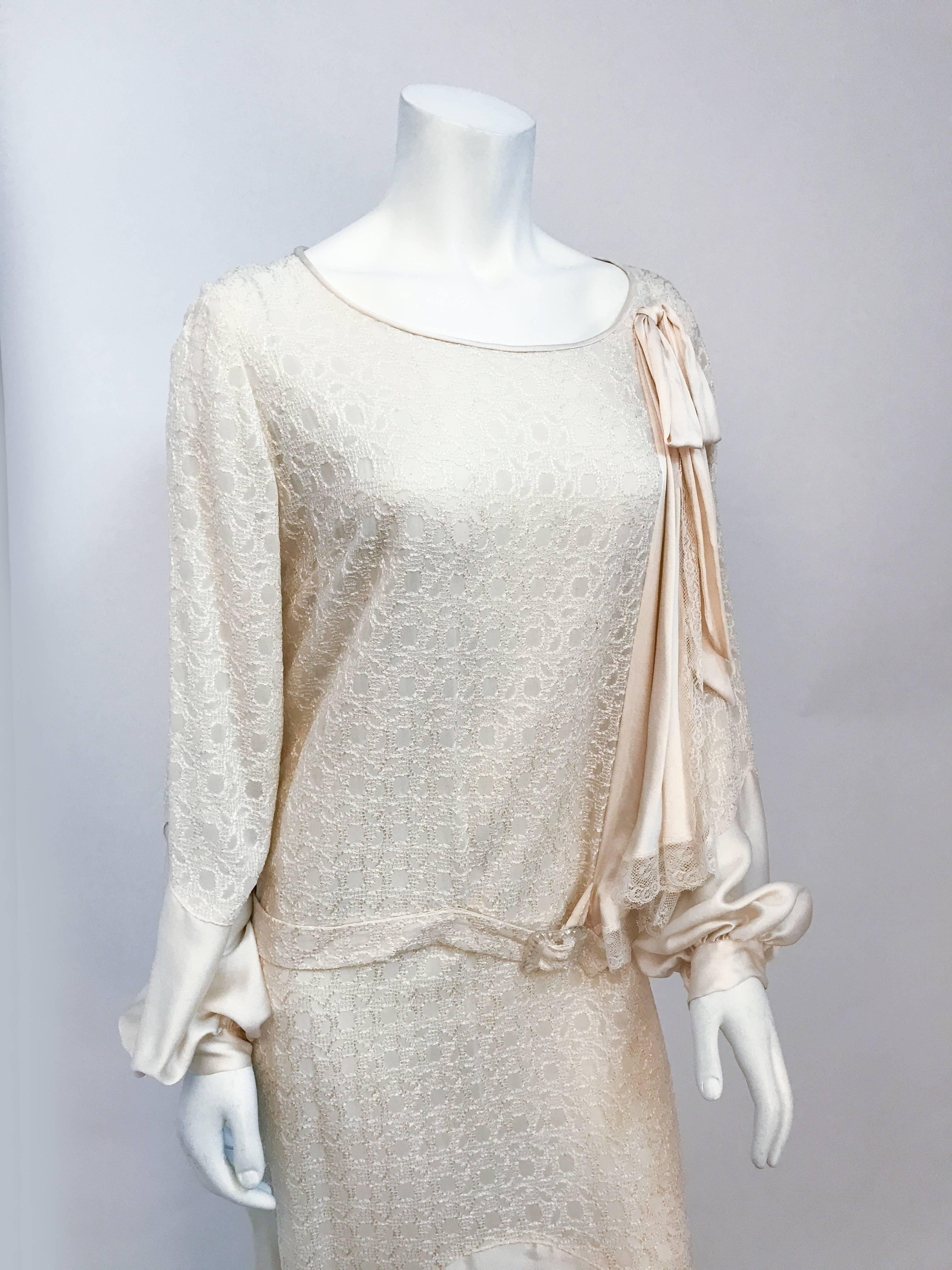 1920s Silk Cream Chiffon and Satin Dress. cream silk chiffon dress with repeated embroidered pattern, long sleeves with snaps near the wrists. Attached belt with clear glass buckle, drop waist, and scoop neck. Multi tiered lace edged asymmetrical