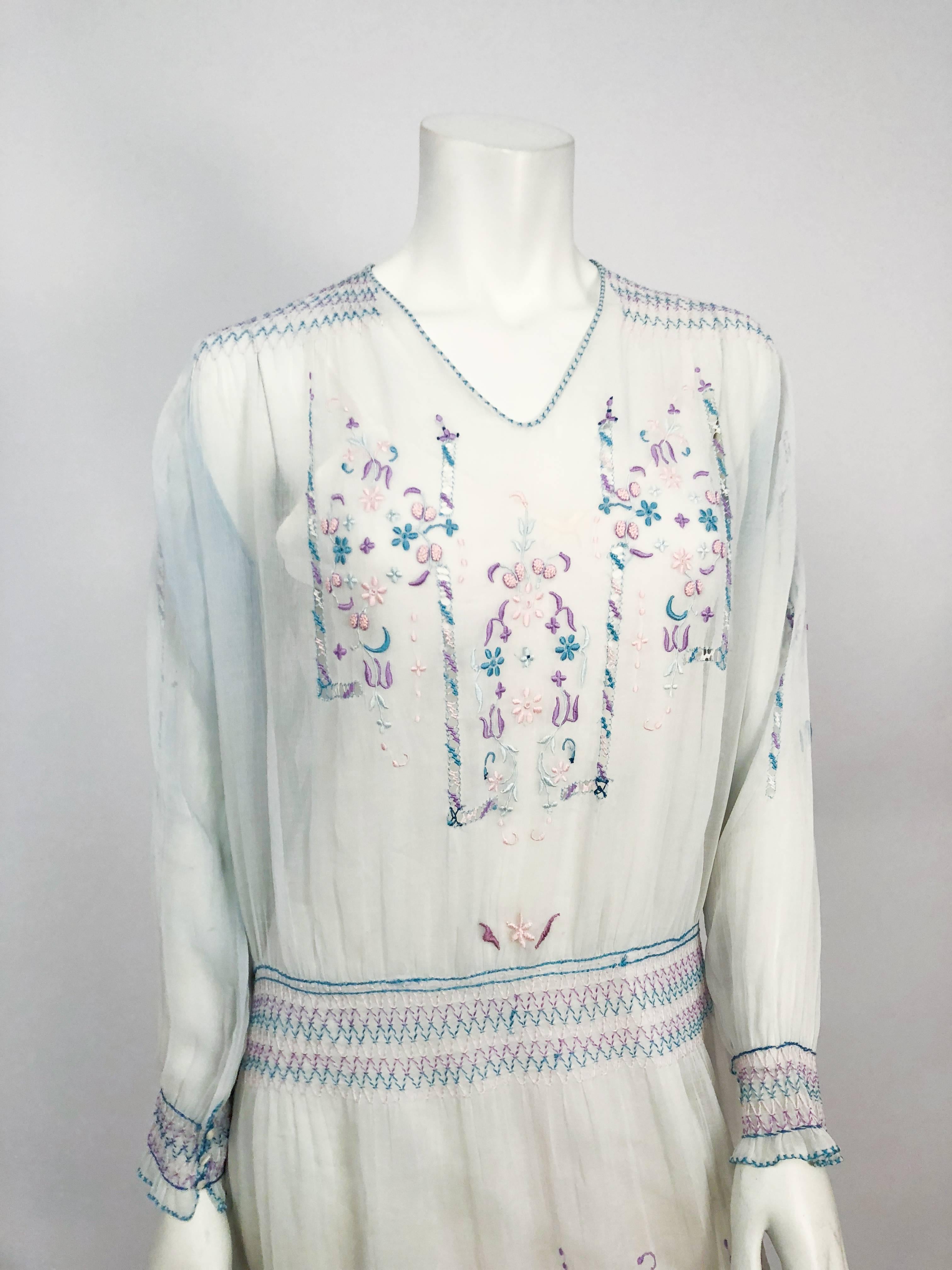 1920s White Cottage Dress with Hand-embroidery and Pull-work. White cottage dress with multicolored embroidery with pull-work and smocking details. Pin-pleats on the back of the neckline. Smocked sleeve cuffs with seashell button closure. Drop