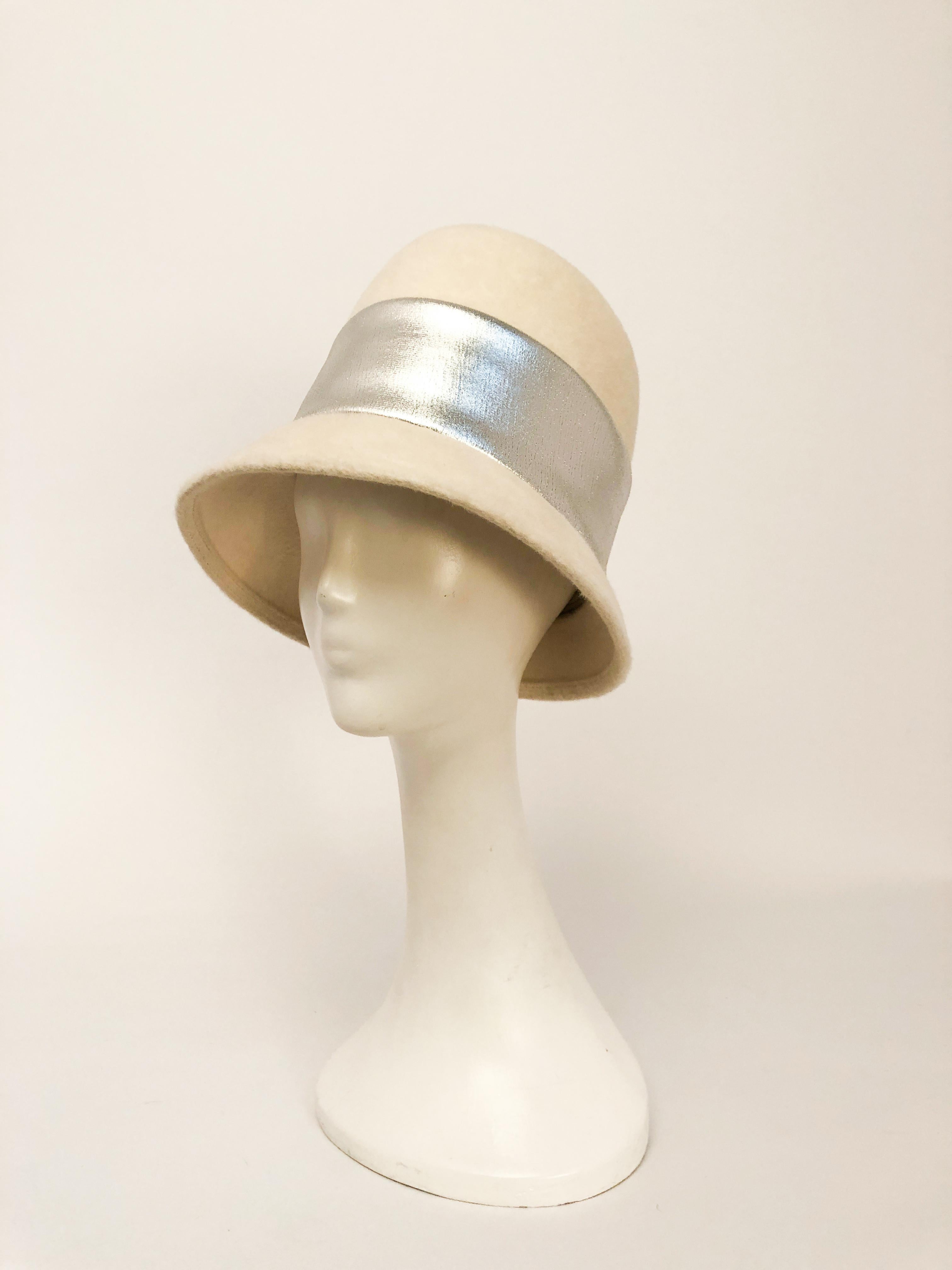 1960er Jahre Creme Mod Hut. Cremefarbener Mod-Biberfilzhut mit extrem hoher Krone, typisch für die High Fashion der 60er Jahre, breitem Silberband mit verdecktem Knopfverschluss auf der Rückseite und nach hinten schmaler werdender Krempe.