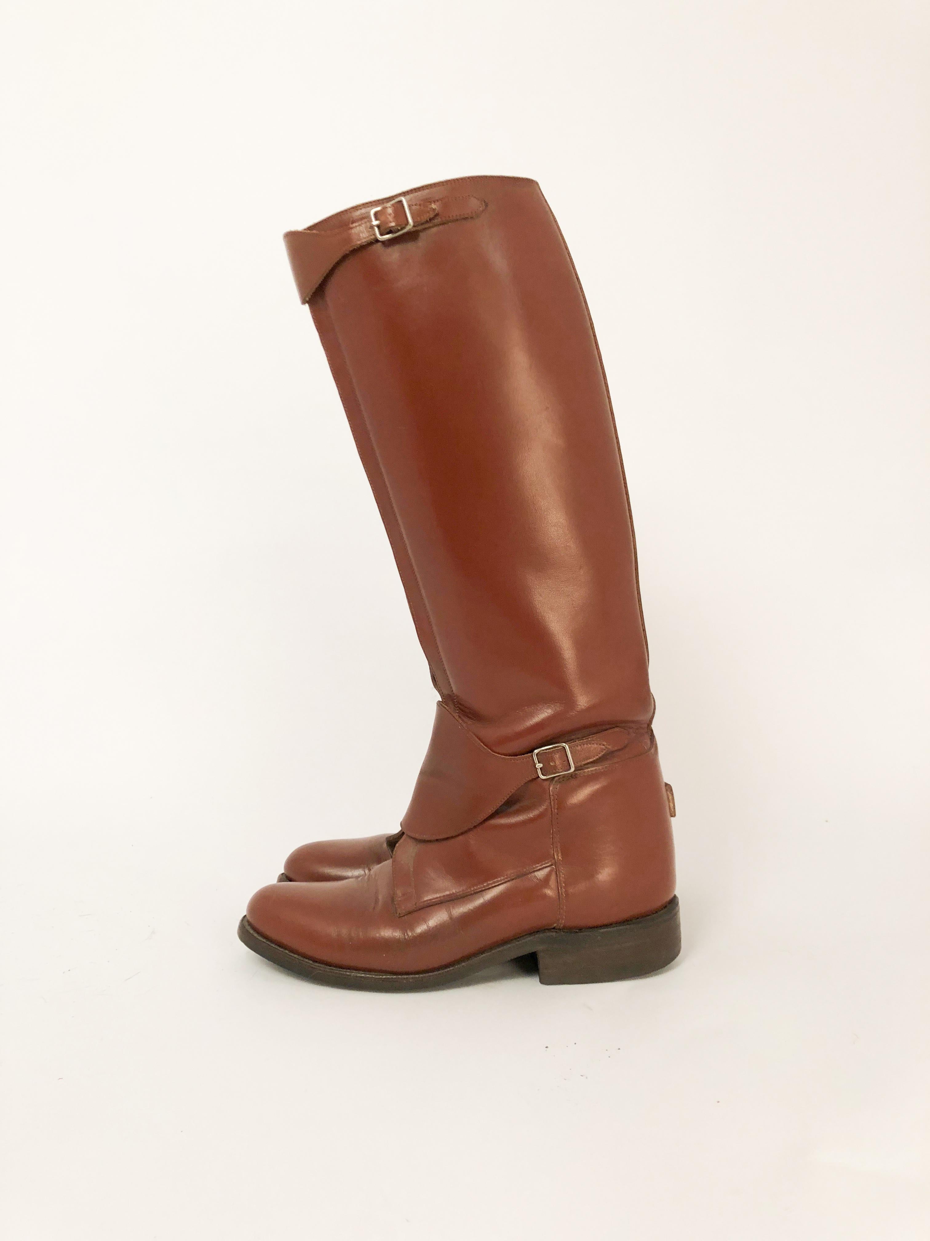 Cordovan colored leather riding boots with pig skin lining, front zipper, curved straps/bucklings on the top and bottoms of the zipper to lock the boots in place. Spur stop on the heel.