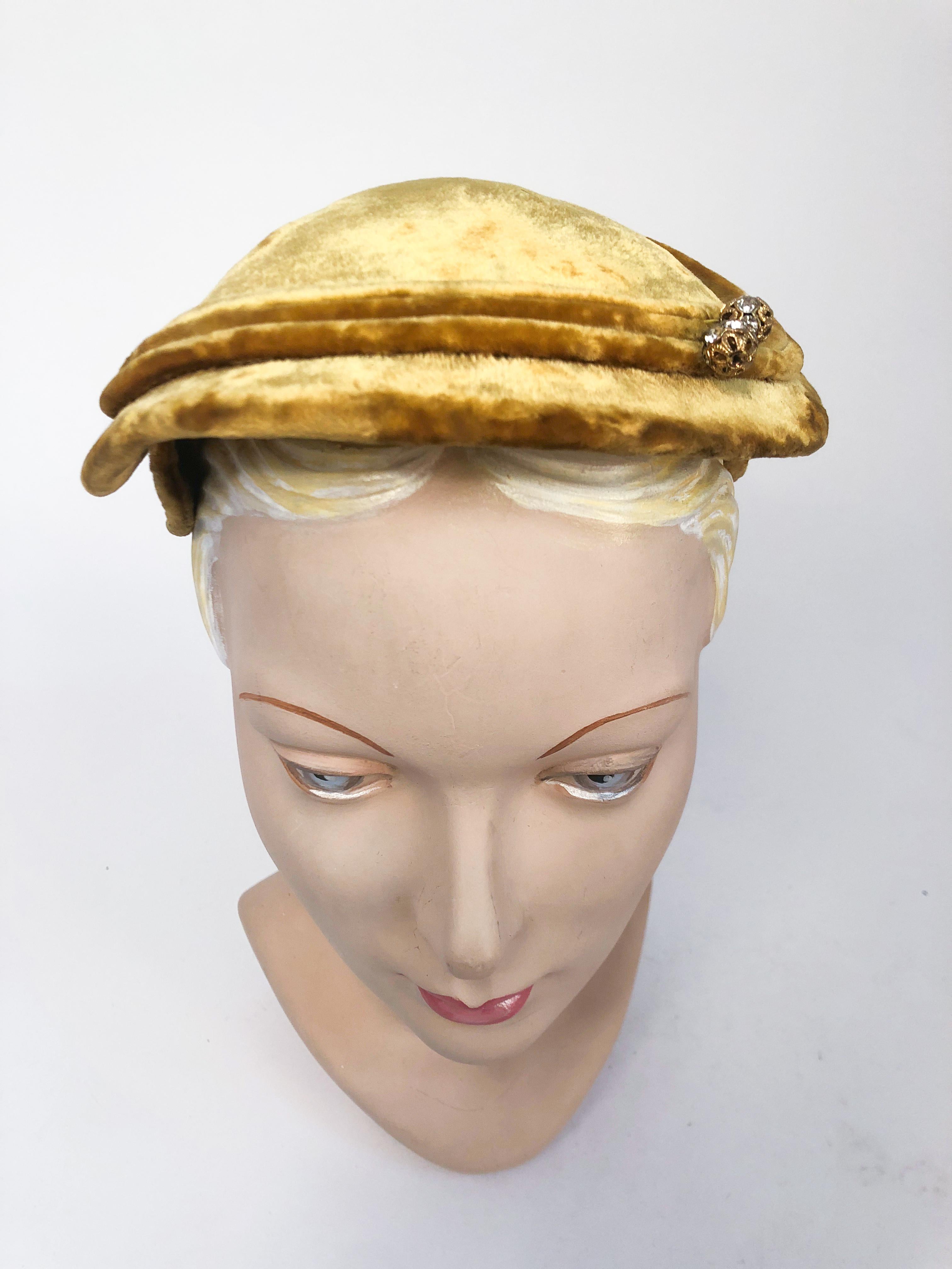 1950s Gold velvet hat with matching corded trim and two brass and rhinestone accent pieces. This hat may also be worn with a decorative hat pin.