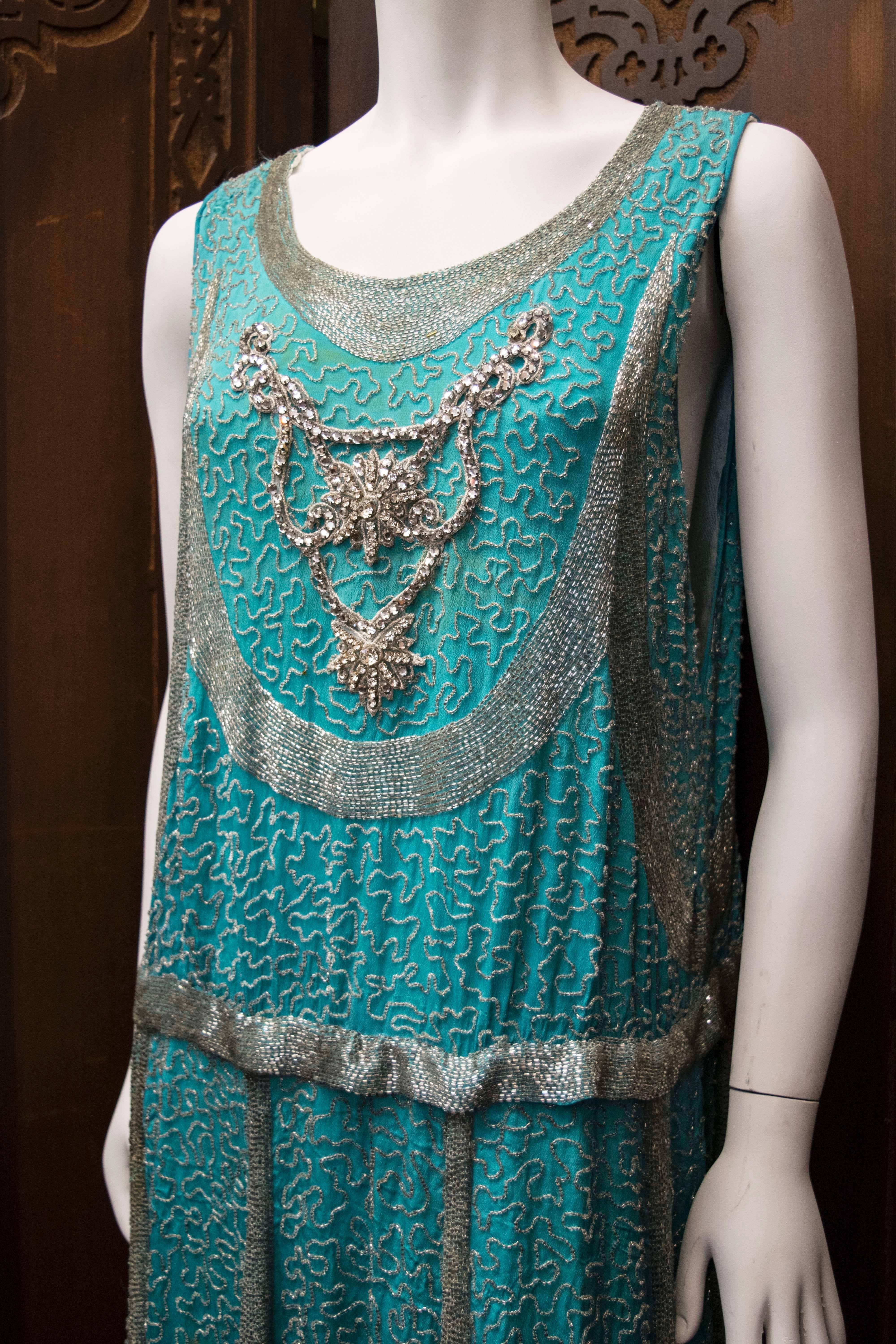 1920s Beaded Aqua Flapper Dress.
A unique and rare coloured 1920s dress, hand beaded with beautiful silver bugle  beads. There is an a-symetircal, scalloped hem with a wonderful weight and movement. It has a replacement interior scaffolding which