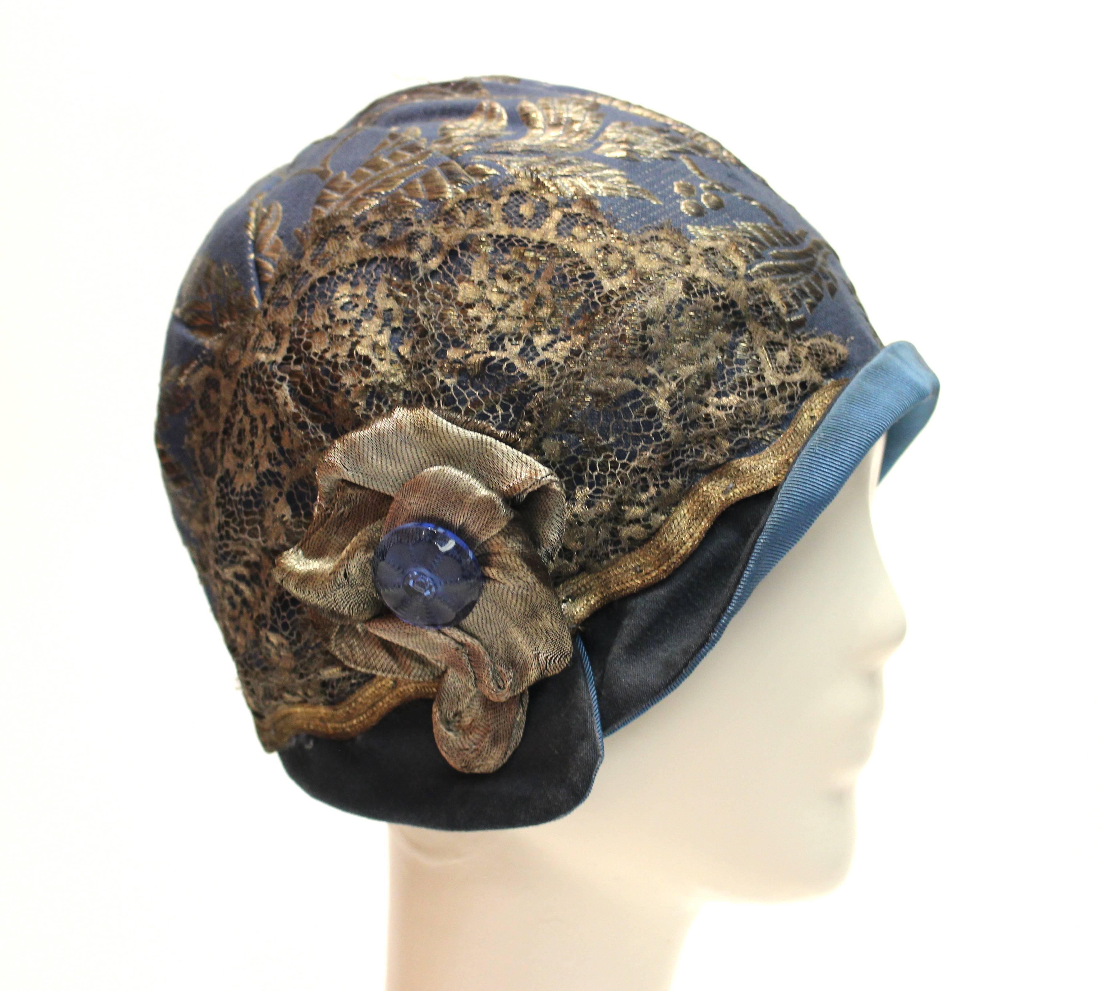 1920s Blue Cloche Hat

Lovely blue 1920s cloche with sterling threads and a silver lamé brocade. There is a metal lace embellishment with glass button detail. This is wearable piece of fashion history. 
The lining is ripped.  

22.5