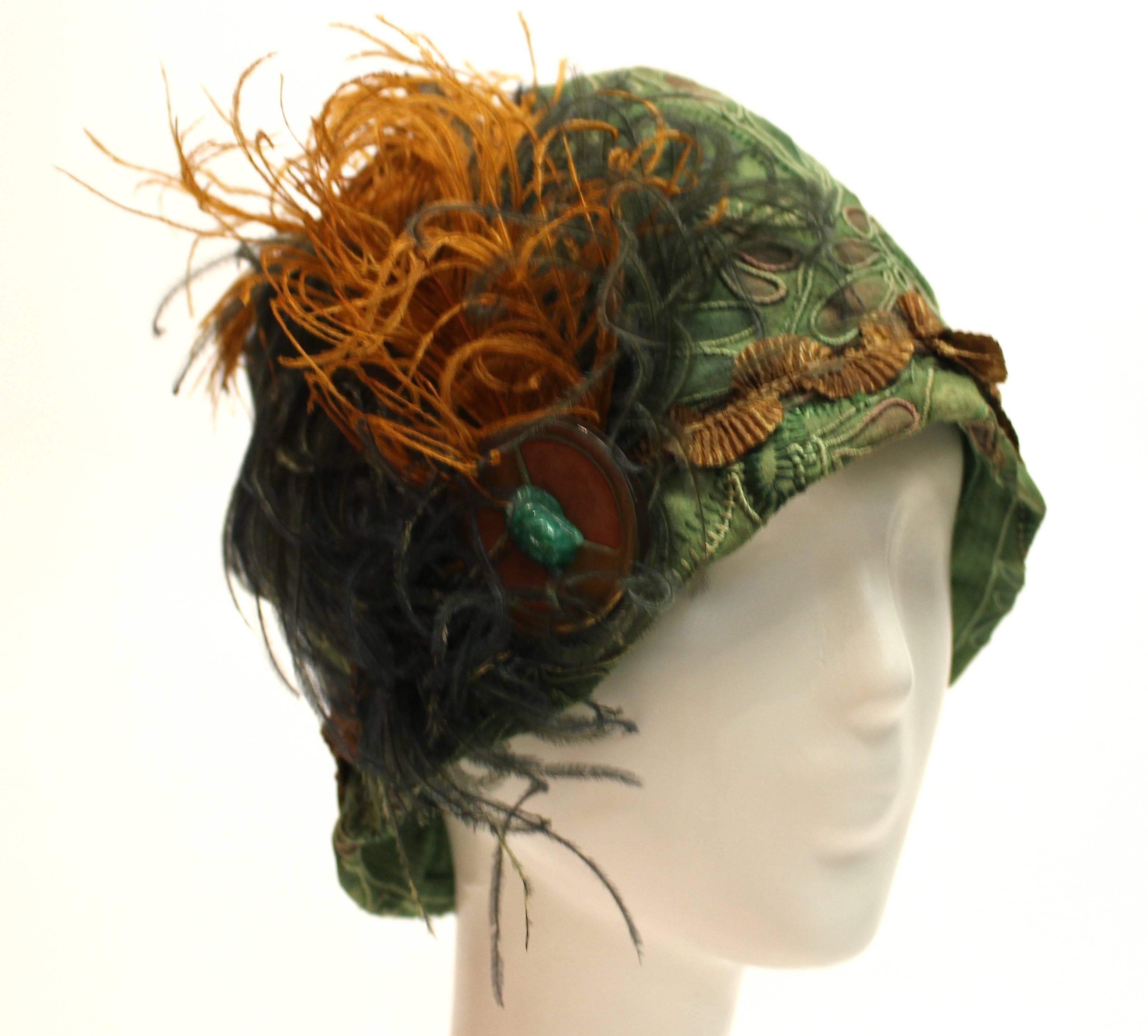 1920s Green Cloche Hat

Beautiful green Cloche hat from the 1920s. It has wonderful soutache detail. It has metallic trim and metal broach with a Pekin glass ornament, and hand curled and dyed ostrich feathers. This piece is a completely wearable