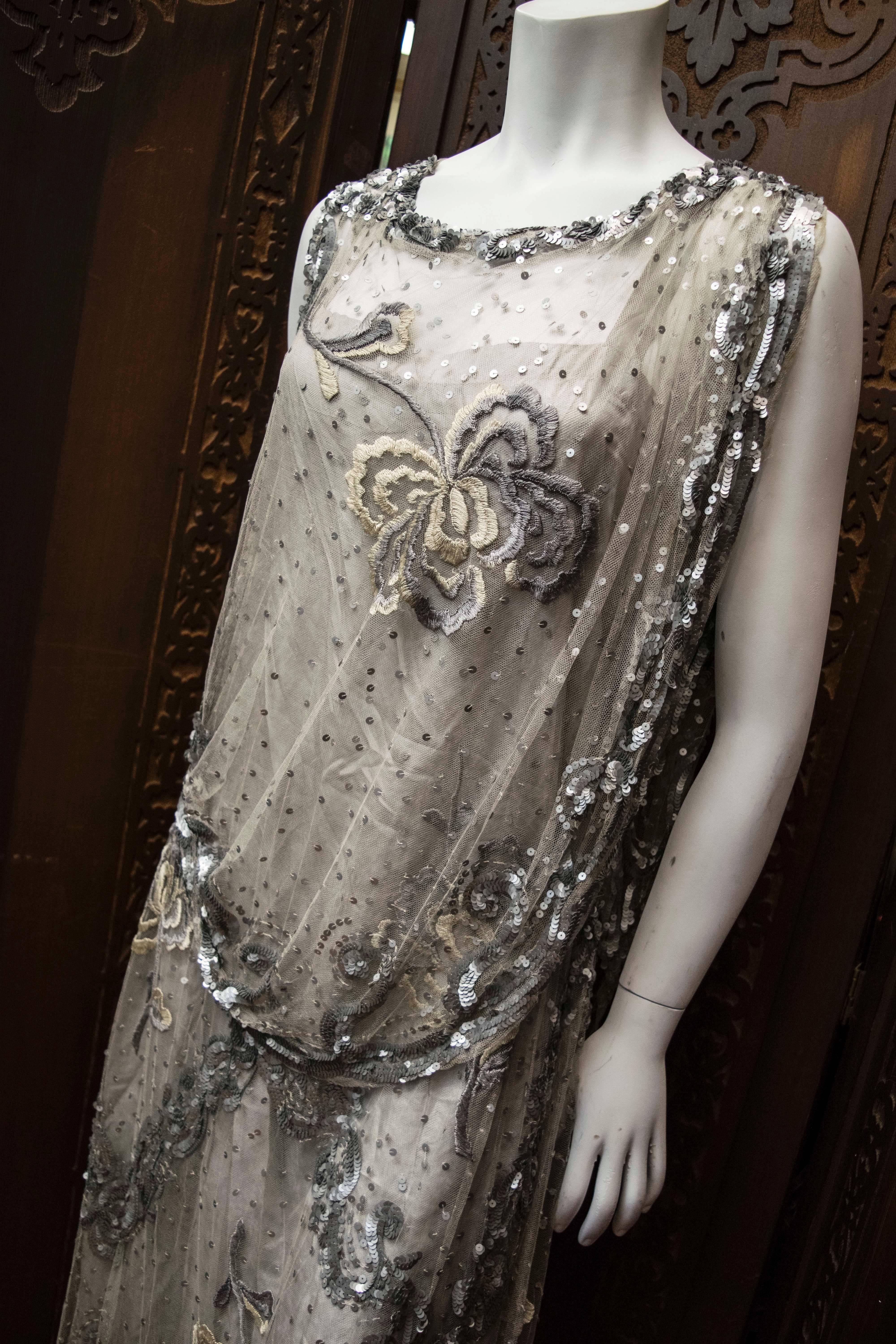 1920s Silver Lace Sequinned Dress

One of the most beautiful 1920s dresses we've ever possessed, completely hand embroidered and hand sequinned with its original silk silver slip. The dress's colour scheme features soft greys, silvers and pewter.