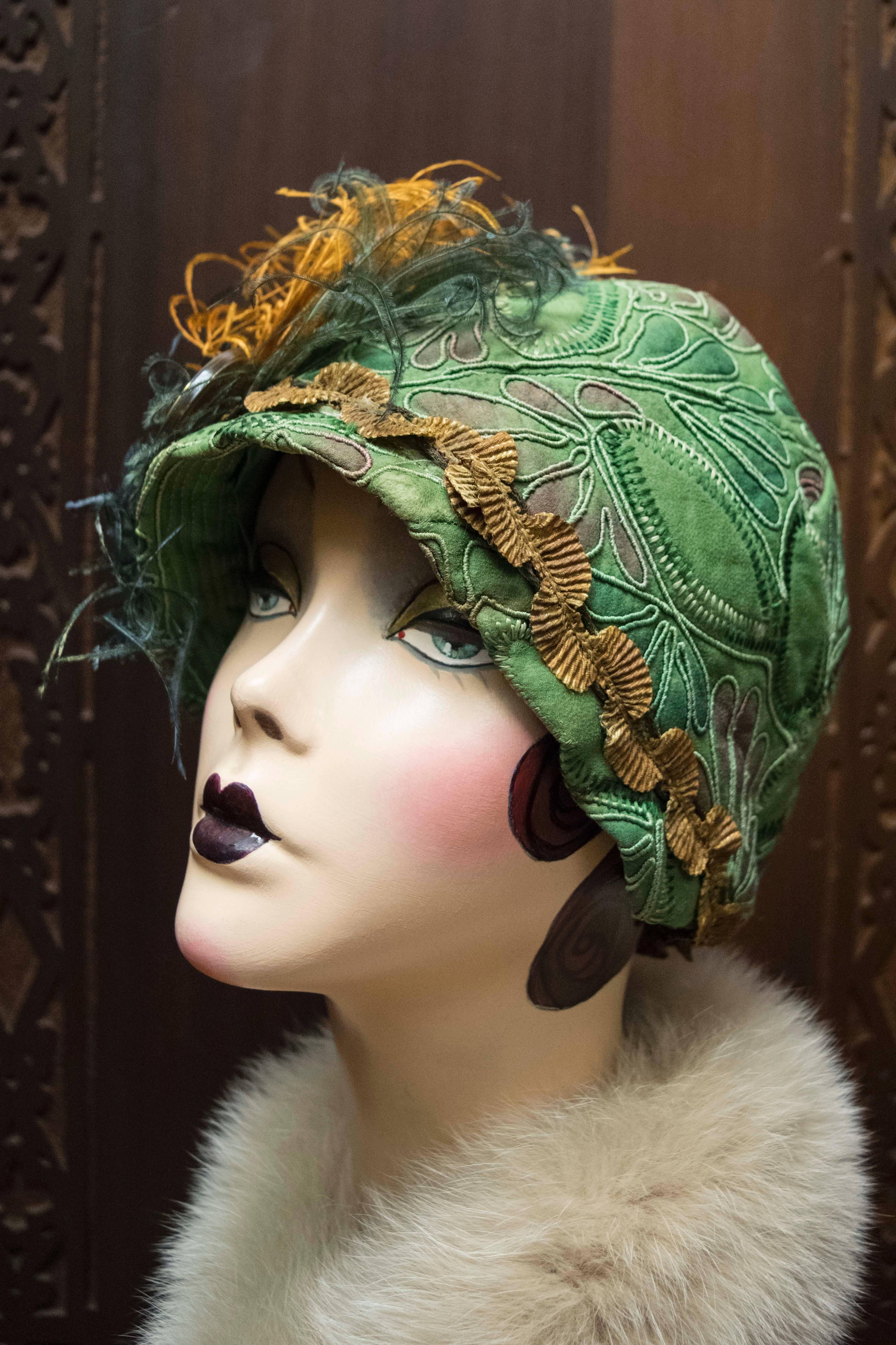 1920s Green Cloche Hat

Beautiful green Cloche hat from the 1920s. It has wonderful soutache detail. It has metallic trim and metal broach with a Pekin glass ornament, and hand curled and dyed ostrich feathers. This piece is a completely wearable