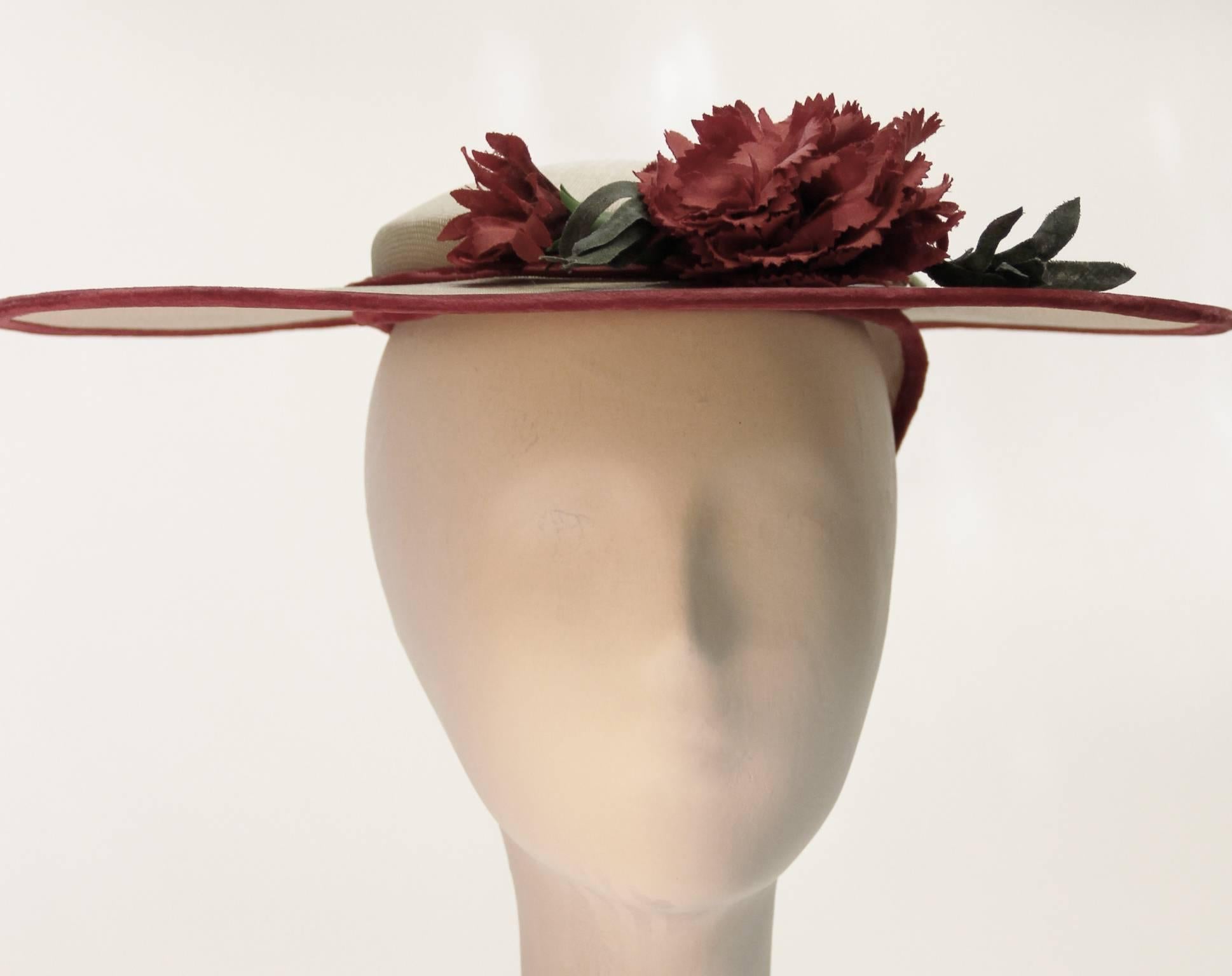 Truly sweet 1950s wide brimmed woven straw sun hat trimmed in red velvet. Adorned with two faux red carnation flowers (green leaves and stems included!) 

 