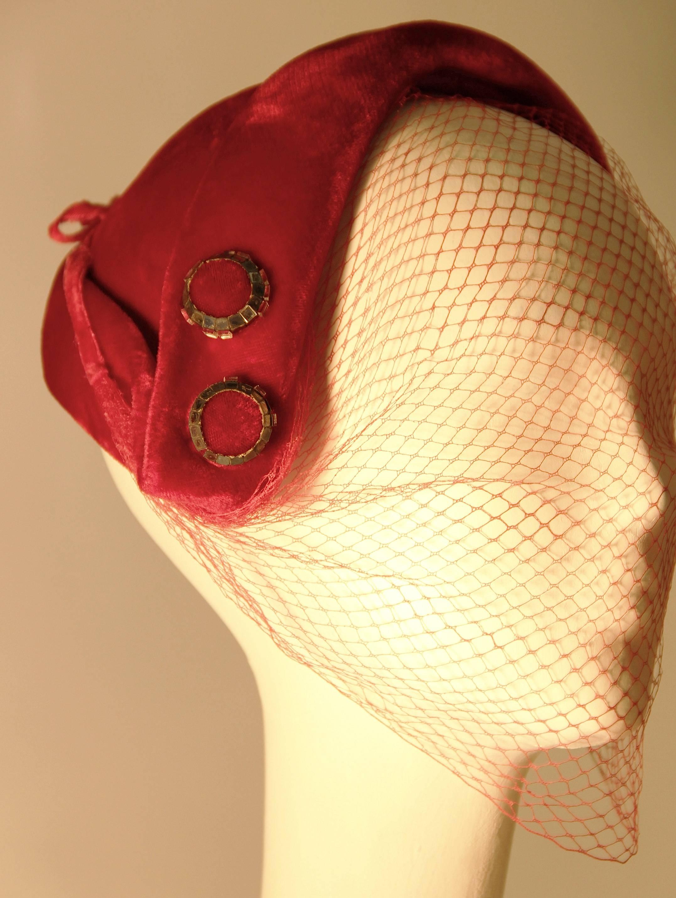 1950s red velvet cocktail hat adorned with two mirror trimmed buttons. Original red veil with velvet ties.  

