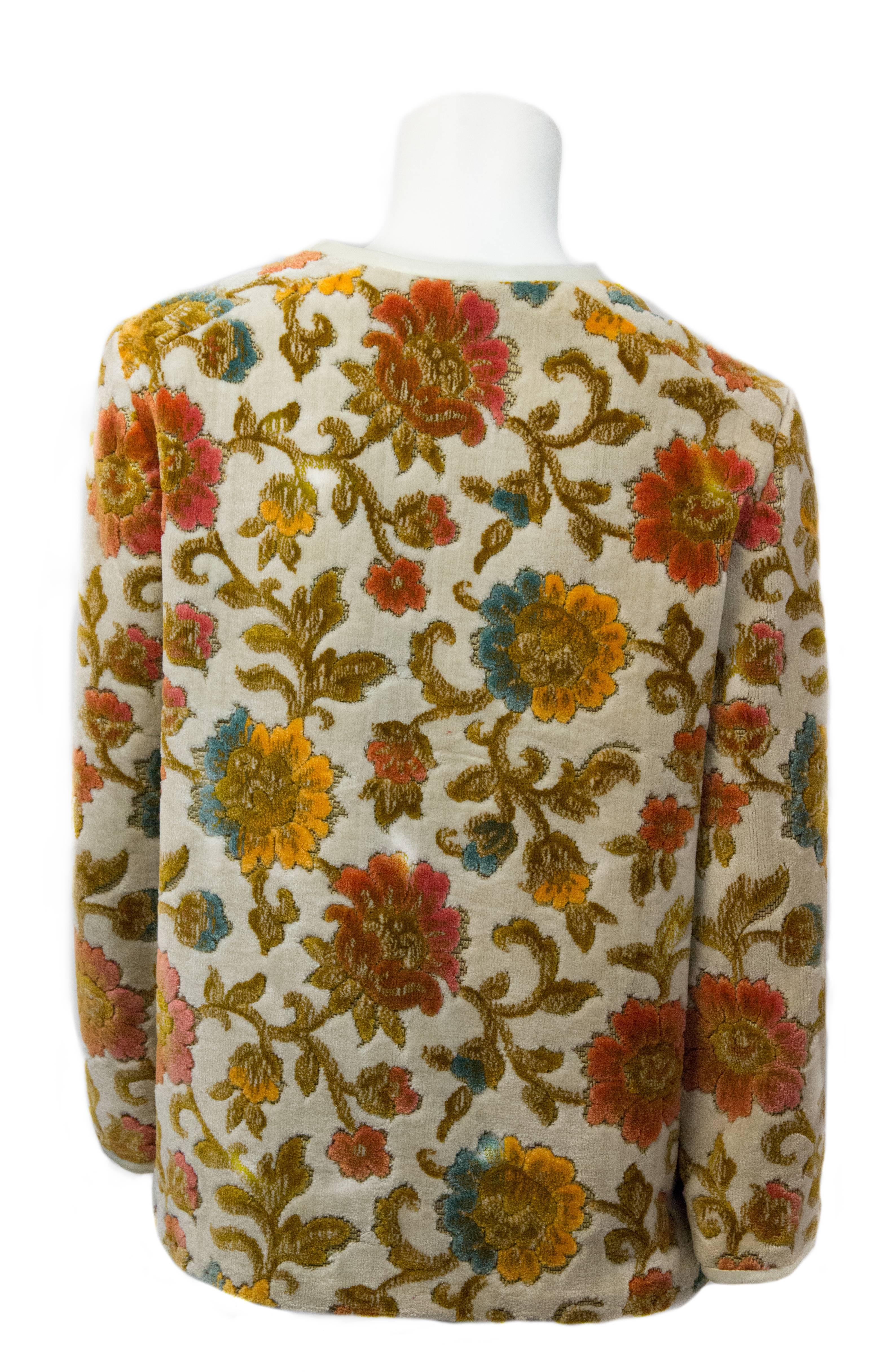 60er-Jahre-Jacke mit geblümtem Wandteppich und weißem Lederbesatz. Metallreißverschluss auf der Vorderseite mit Lederquaste als Zugband. Flache Vordertaschen. Gefüttert mit Satin. 