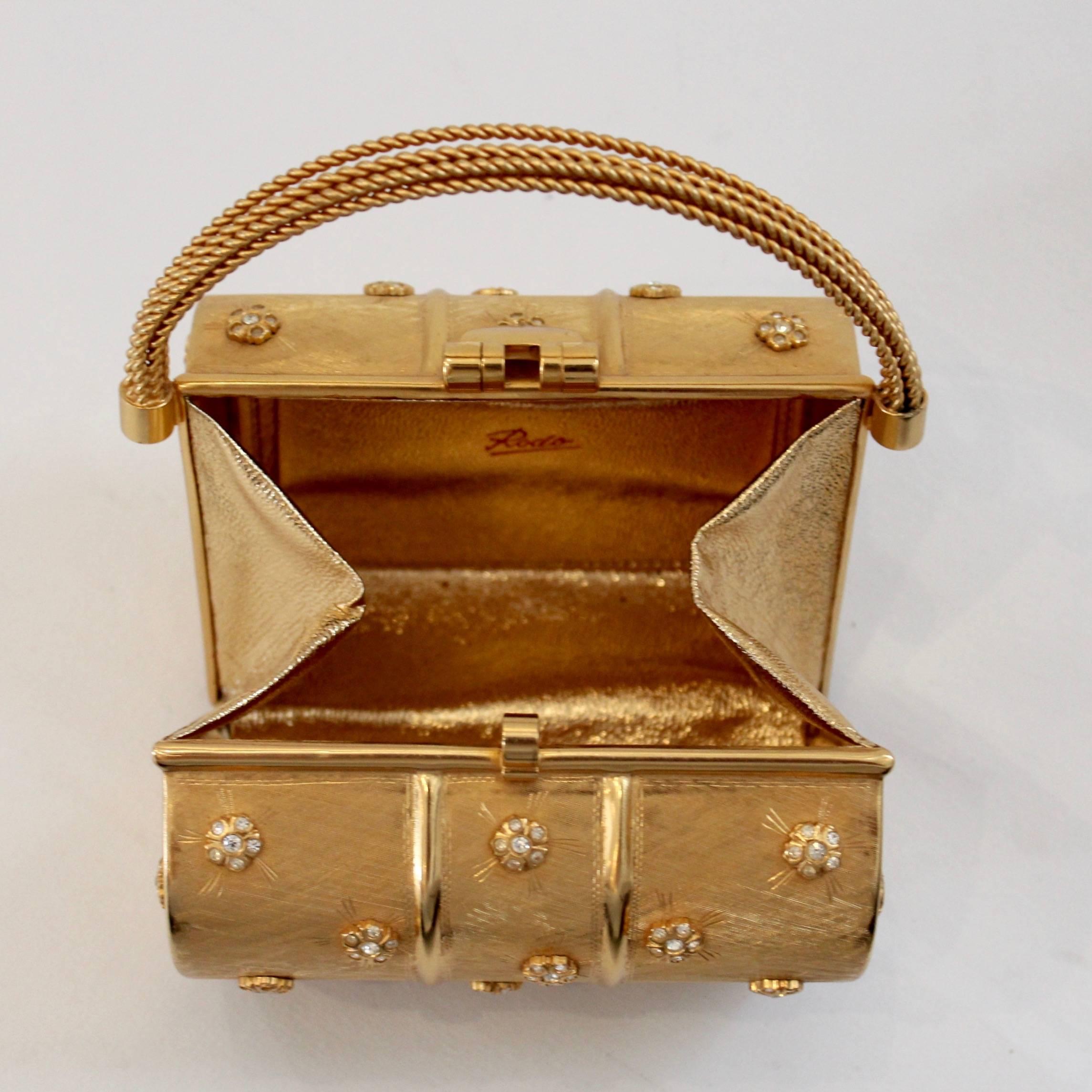 This square gold Rodo evening bag is a 1970s treasure. This structured boxed bag is decorated with small rhinestones and features a woven metal handle. The interior is gold lined and includes a pocket for your smallest possessions. A snap down clip