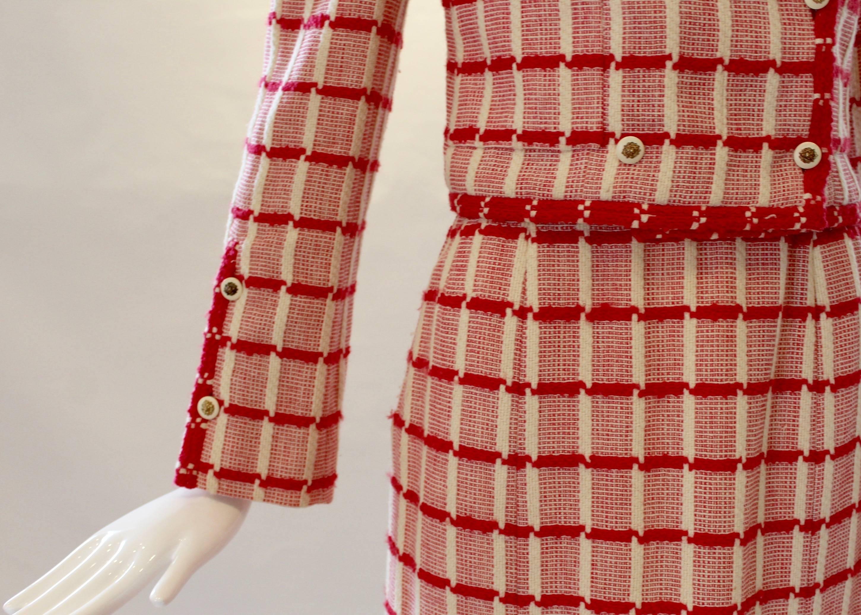 A rare vintage find! This chic skirt suit from Chanel boasts a red and cream grid pattern and is finished with signature Chanel lion’s head buttons. It includes a jacket with front pockets and button closure and a high-waisted knee-length pleated