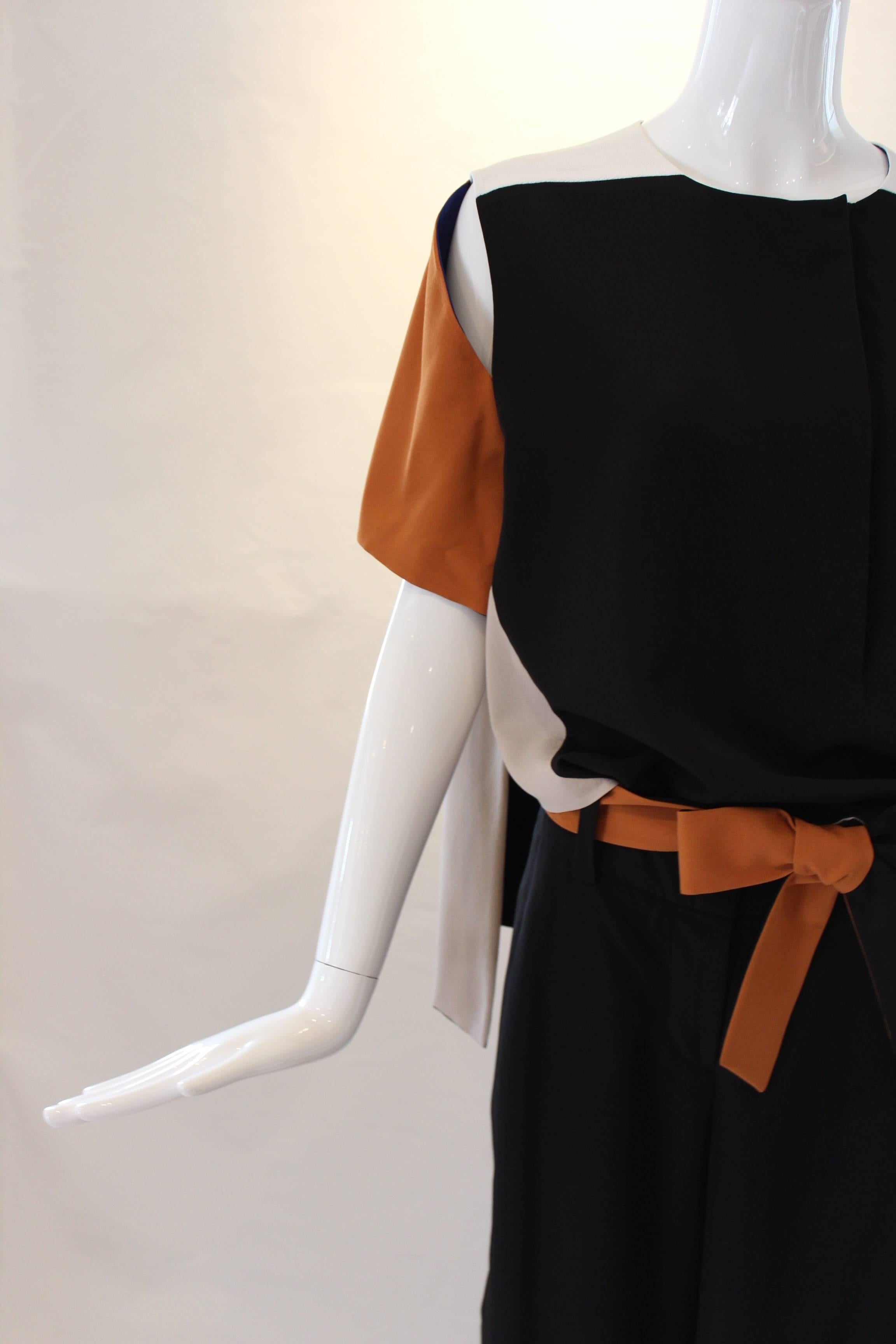 This beautifully tailored 1980s Thierry Muglar Pant Suit boasts high waisted black wide-leg trousers with a contrasting burnt orange belt. The matching color blocked top has tasteful cutouts at the shoulder with a cape-like detail at the back. A
