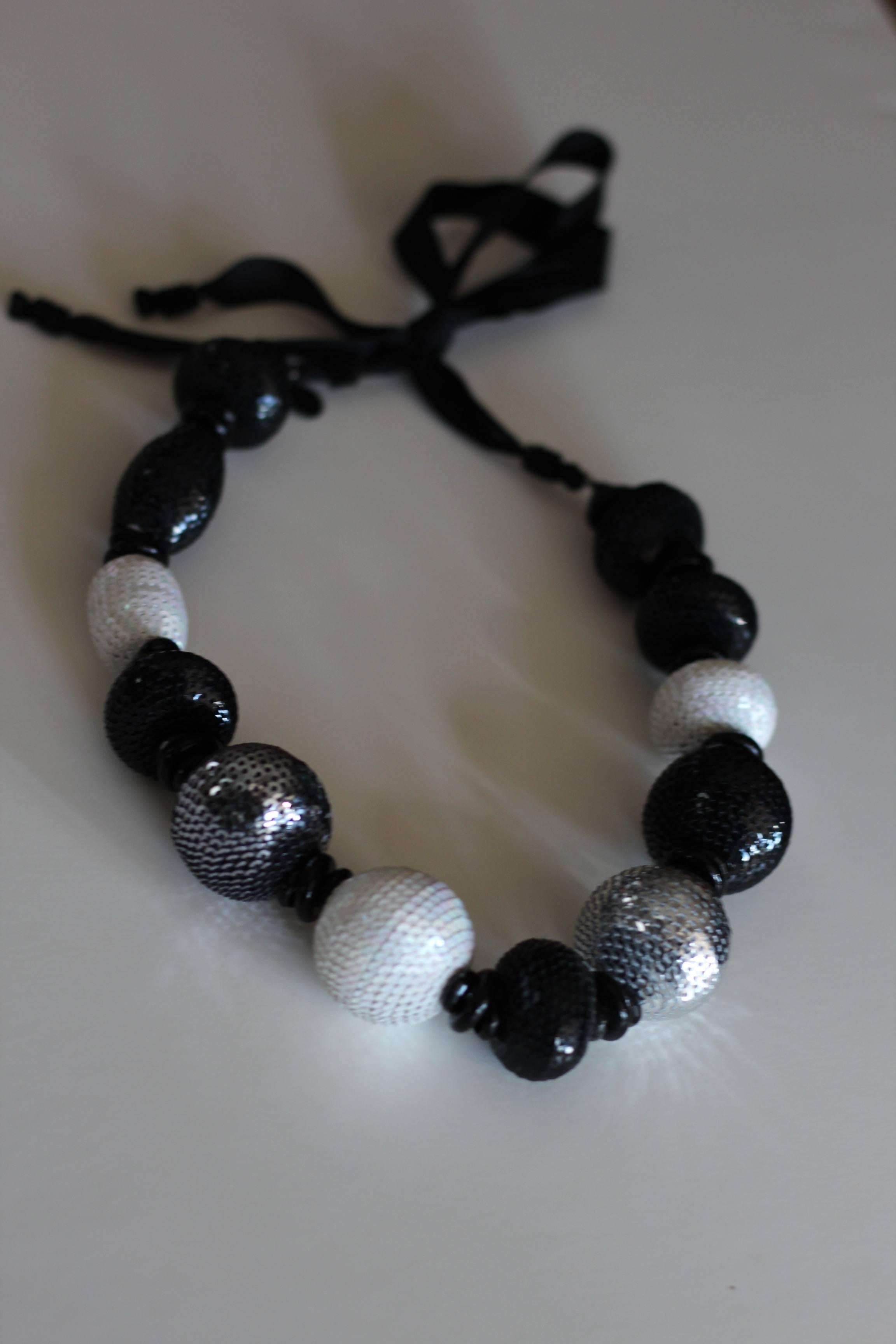 Shine bright this holiday season in this stunning 1980s Gucci Paillette Ball Necklace. Hand sewn piallettes in shades of black, silver and white decorate various sized balls in this statement necklace. Tied together with a black grosgrain ribbon,