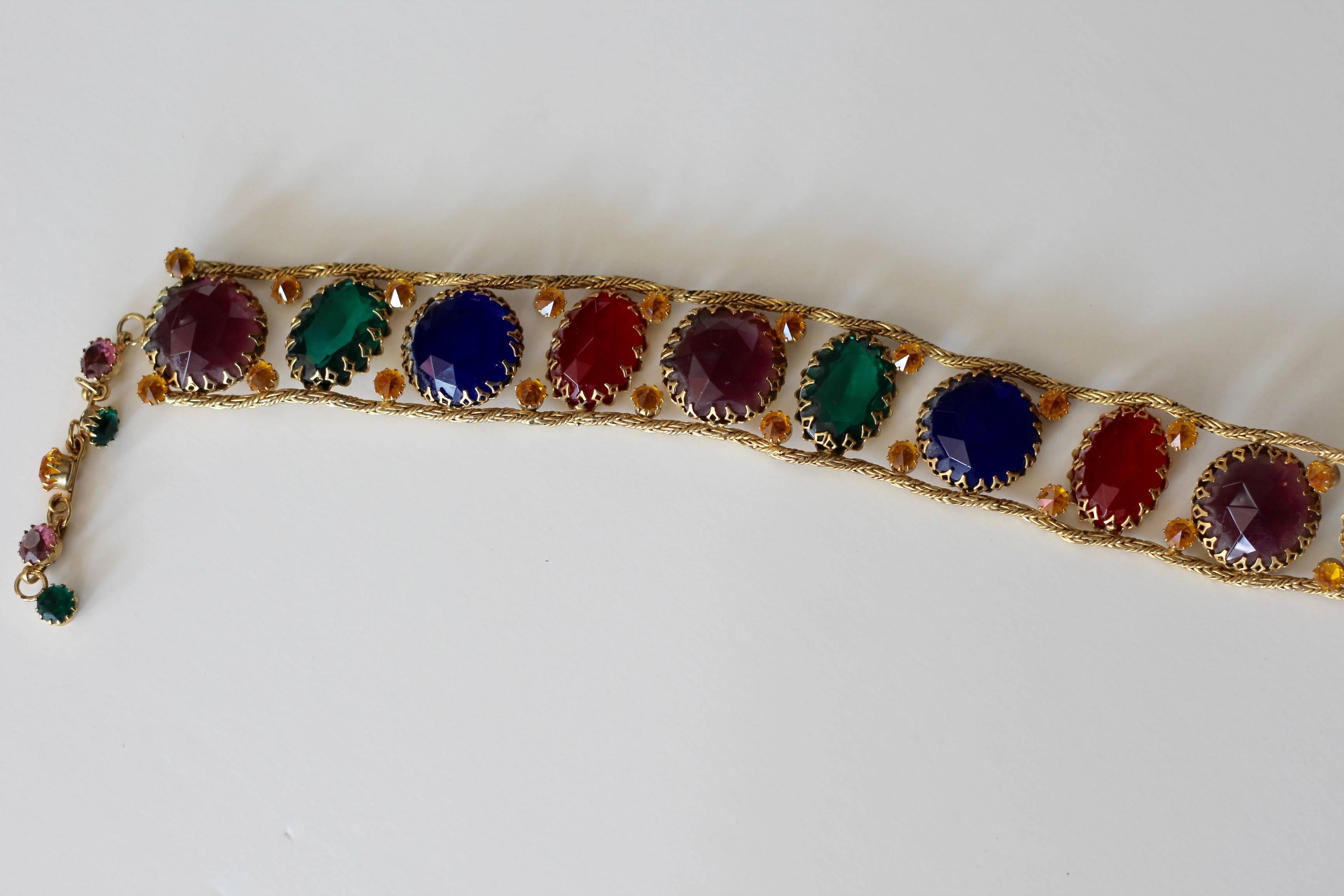 1960s glamourous gold toned, multicolored jeweled belt unsigned by Schreiner of New York. Has round and oval shaped faceted faux gemstones in varying sizes and colors; red, amber, green, blue, and lavender. Stones are joined together by gold toned