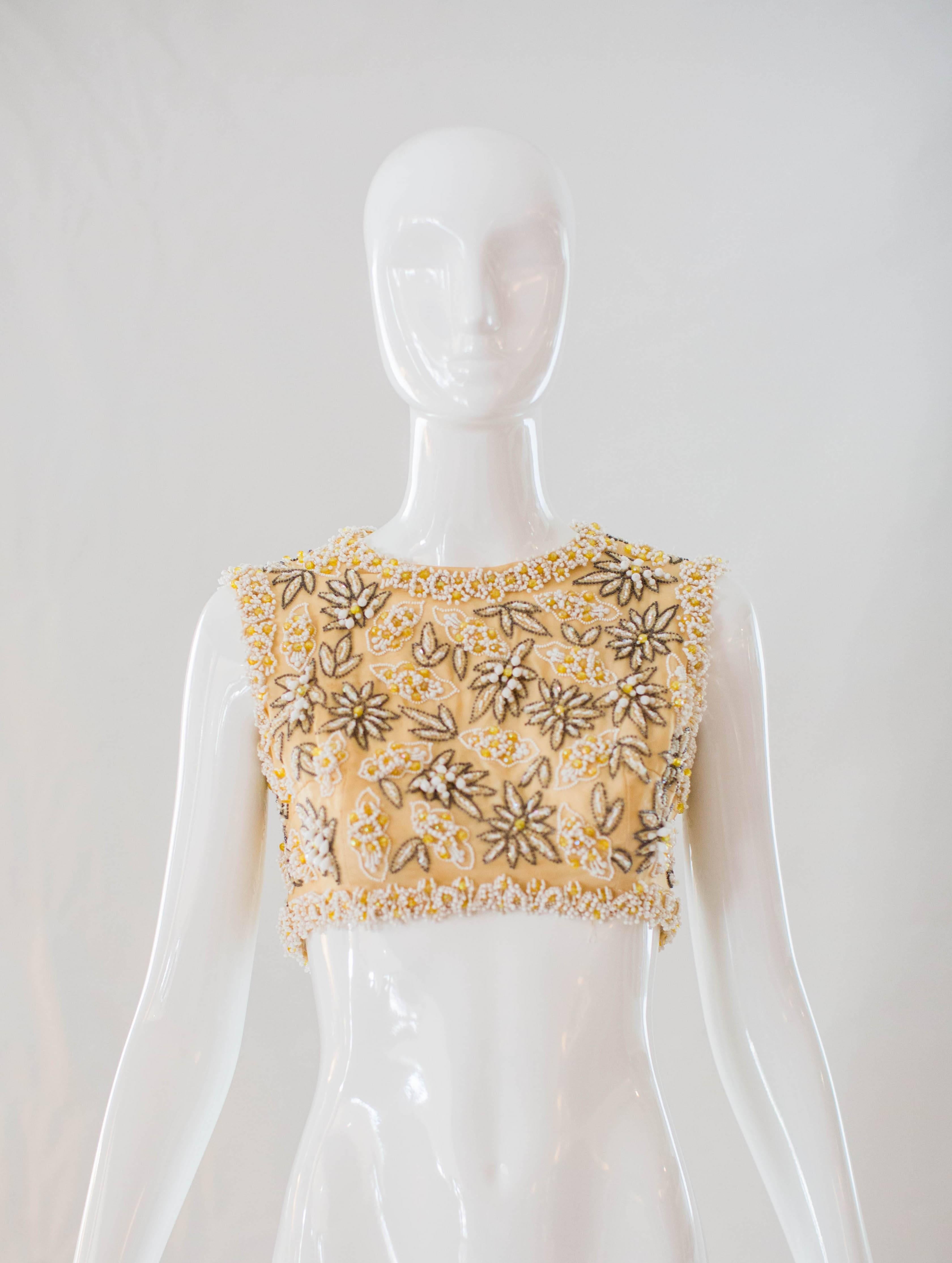 This stunning crop top is decorated with glass beaded details on shades of yellow, ivory and silver. Paired with high waisted pants or a full skirt, there are many different ways to style this statement stunner. The back features a hidden zipper