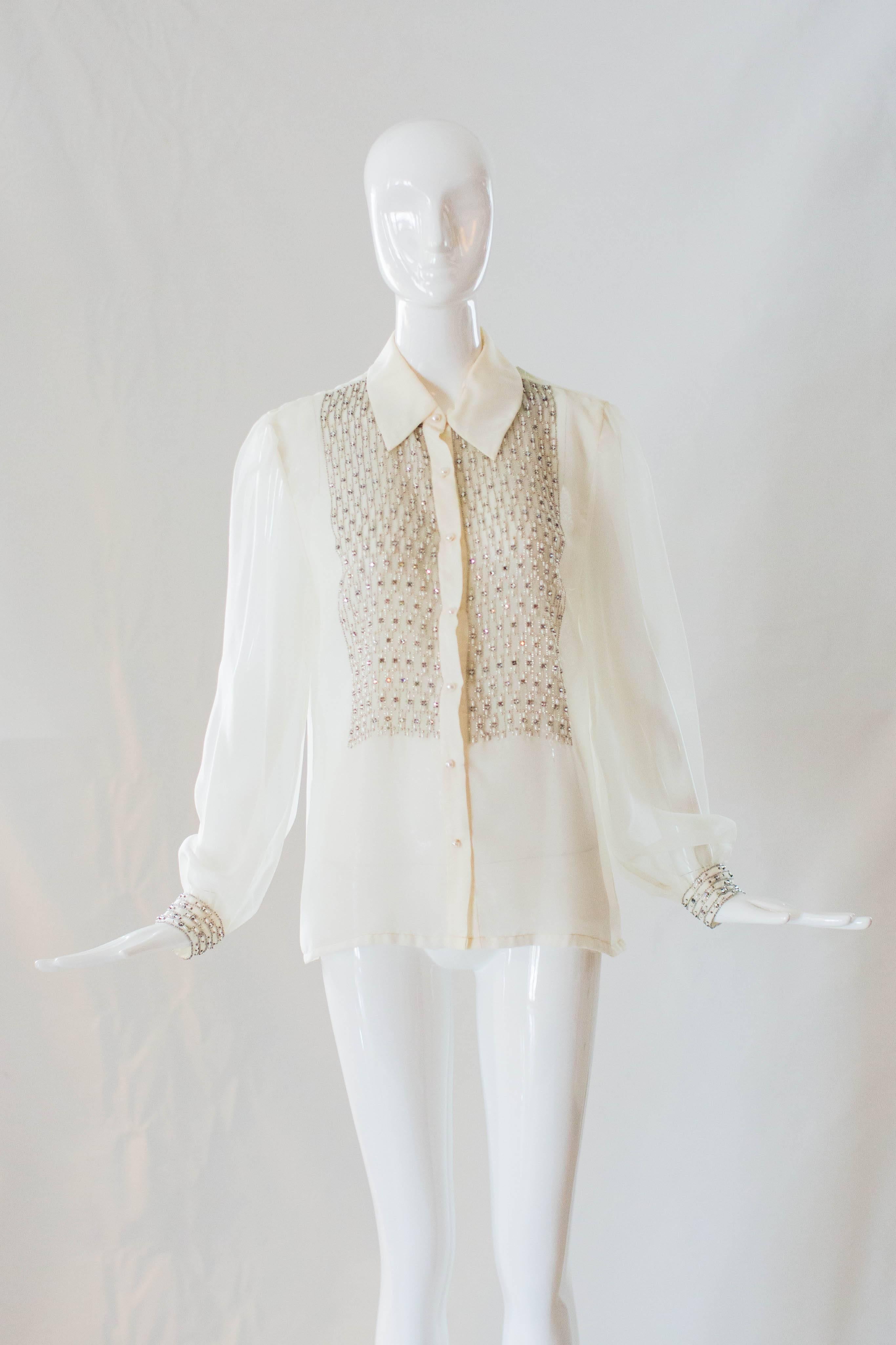 This 1960s Victoria Royal beaded blouse comes in a silhouette that will never go out of style! Gorgeous glass beaded details adorn the chest and cuffs of this cream blouse. With a large collar and faux pearl buttons down the chest, this blouse makes