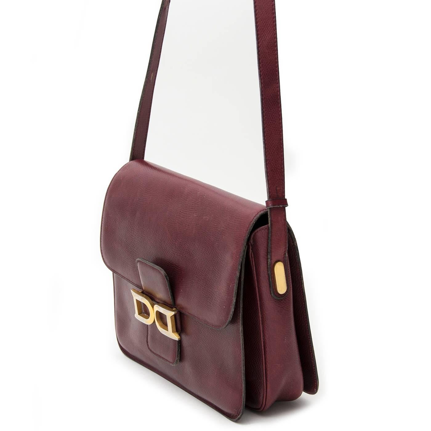 Este clásico Delvaux se presenta en un elegante cuero de color burdeos y cuenta con un cierre de doble D dorada. La bandolera tiene una correa ajustable, por lo que es fácil de llevar colgada del hombro o cruzada. El interior de esta sencilla
