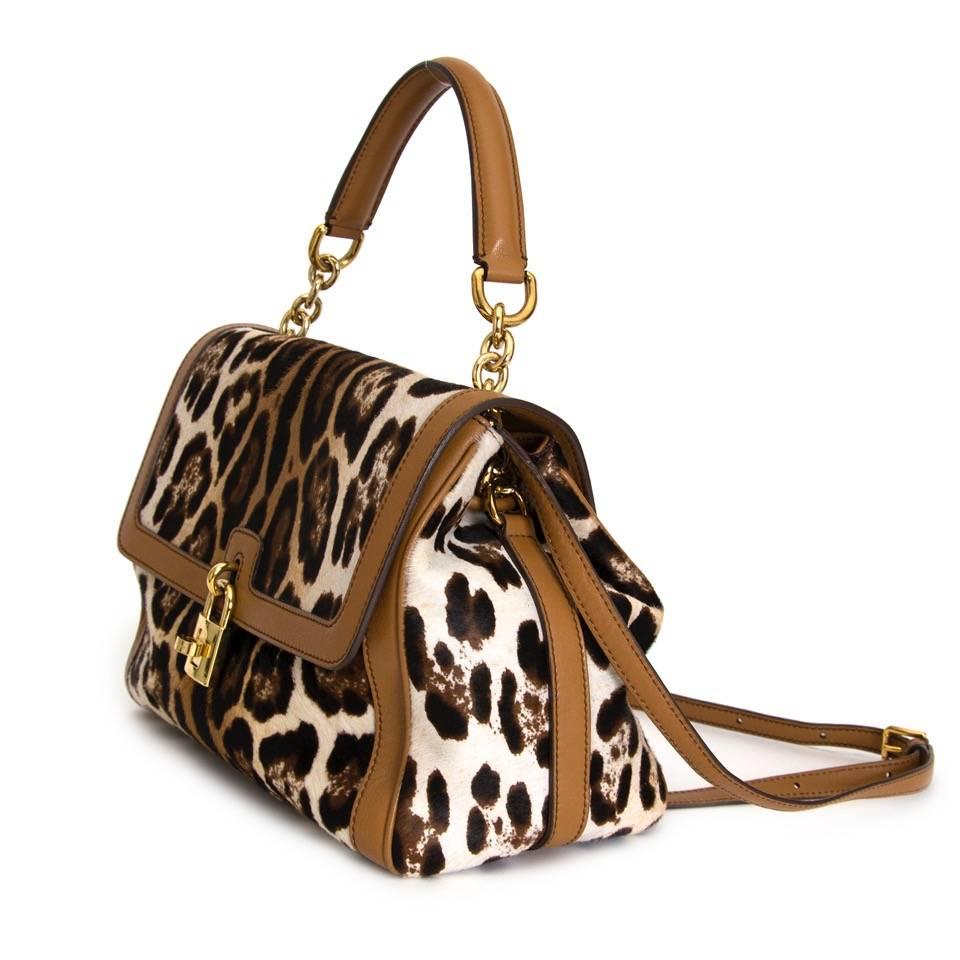 Leopard printed ponyhair bag from Dolce & Gabbana featuring cognac leather , a flap design with a gold-tone padlock fastening, black trims, a leather handle with gold-tone chain details and a detachable shoulder strap. 
The interior features a zip