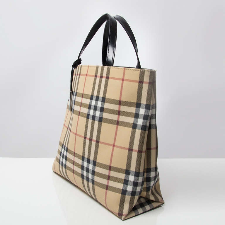 Burberry coated canvas handbag with distinctive tartan pattern. Magnetic snap closure. The interior features a zipped pocket. Silver logo hangtag attached to the handle.