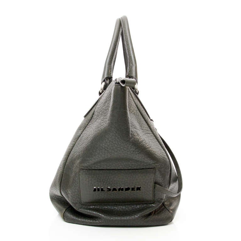 Jill Sander large leather bag in a dark green color. Silver hardware. Large zipper in the middle.

Large Jill Sander logo at the right side with mirror detailing.

The interior features an open pocket and a zipped pocket.

Comes with the