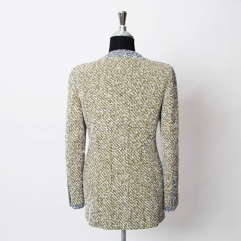 Chanel yellow tweed jacket with zigzag pattern. Blue tweed detailing near the buttons, the pockets and the sleeves. Features two smaller pockets near the chest and two larger pockets below. Large silver tone buttons featuring the 