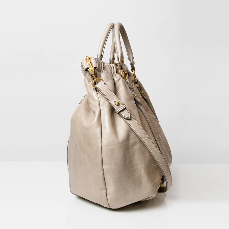 This is an authentic MIU MIU Leather Vitello Lux Gathered Tote in light grey. This ultra-stylish tote is crafted of polished vitello deerskin leather with a cinched top and pleated leather. The bag features rolled leather top handles with an