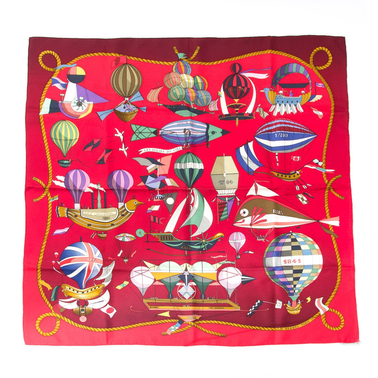 This Hermès carré is a silk scarf designed by Loïc Dubigeon, namde 'Les Folies Du Ciel' depicting airballoons and other 19th century aircrafts. In beautiful deep ombre red.