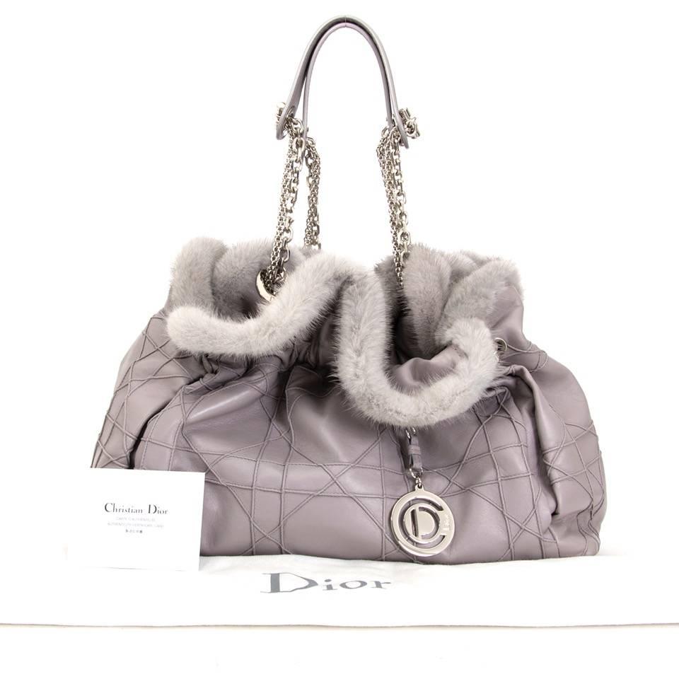 This Christian Dior shoulder bag is a true elegance, detailed with fur and silver hardware. The leather surface comes in a light grey with a subtle hint of purple. The interior opens with magnetic press button and contains one zip, and two slip