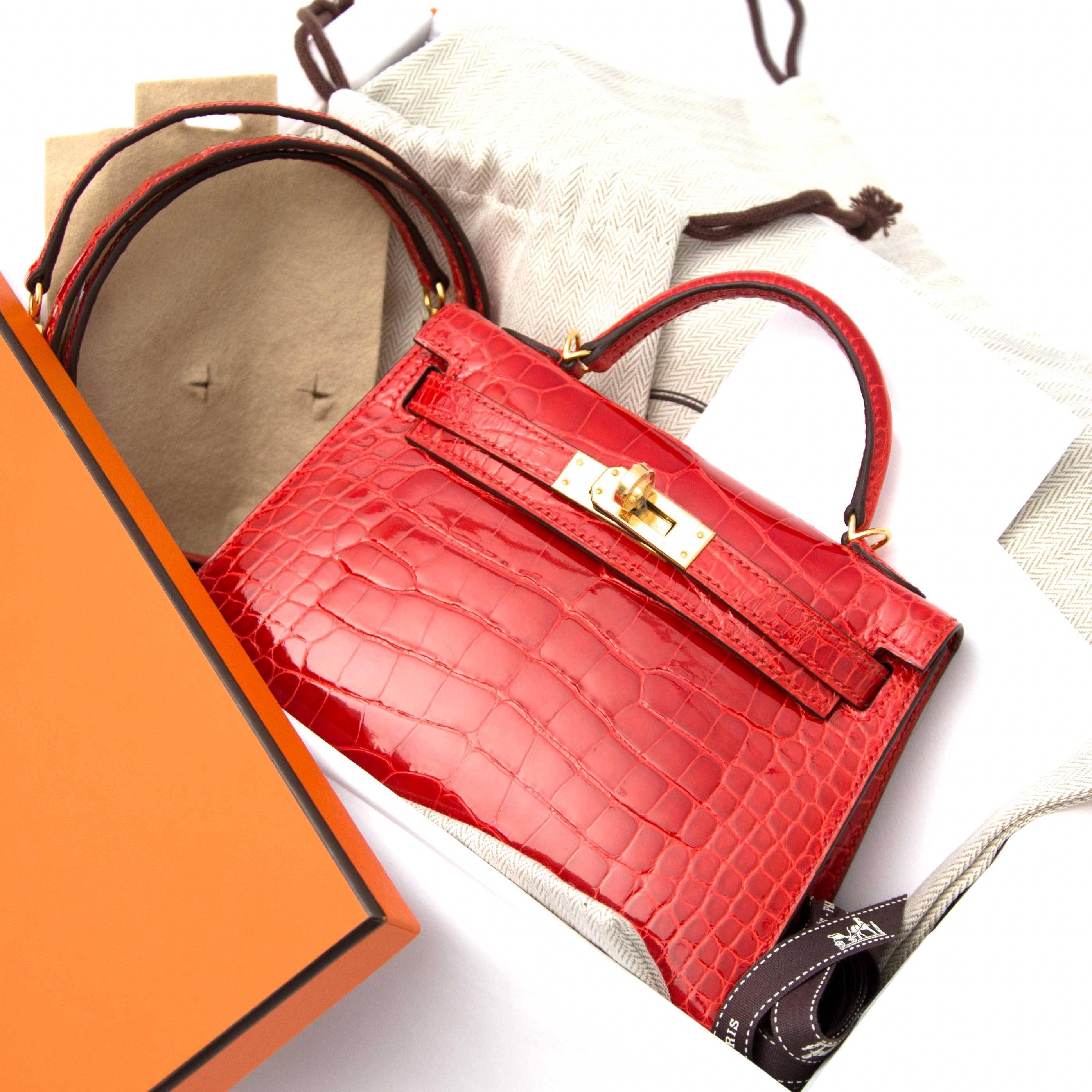 This exquisite hard to find Hermès Kelly Mini Pochette comes in a shiny alligator leather in Vibrant red toned "geranium" color. The alligator mississippiensis skin is identified by the embossed square signature.The Hermes Kelly Pochette