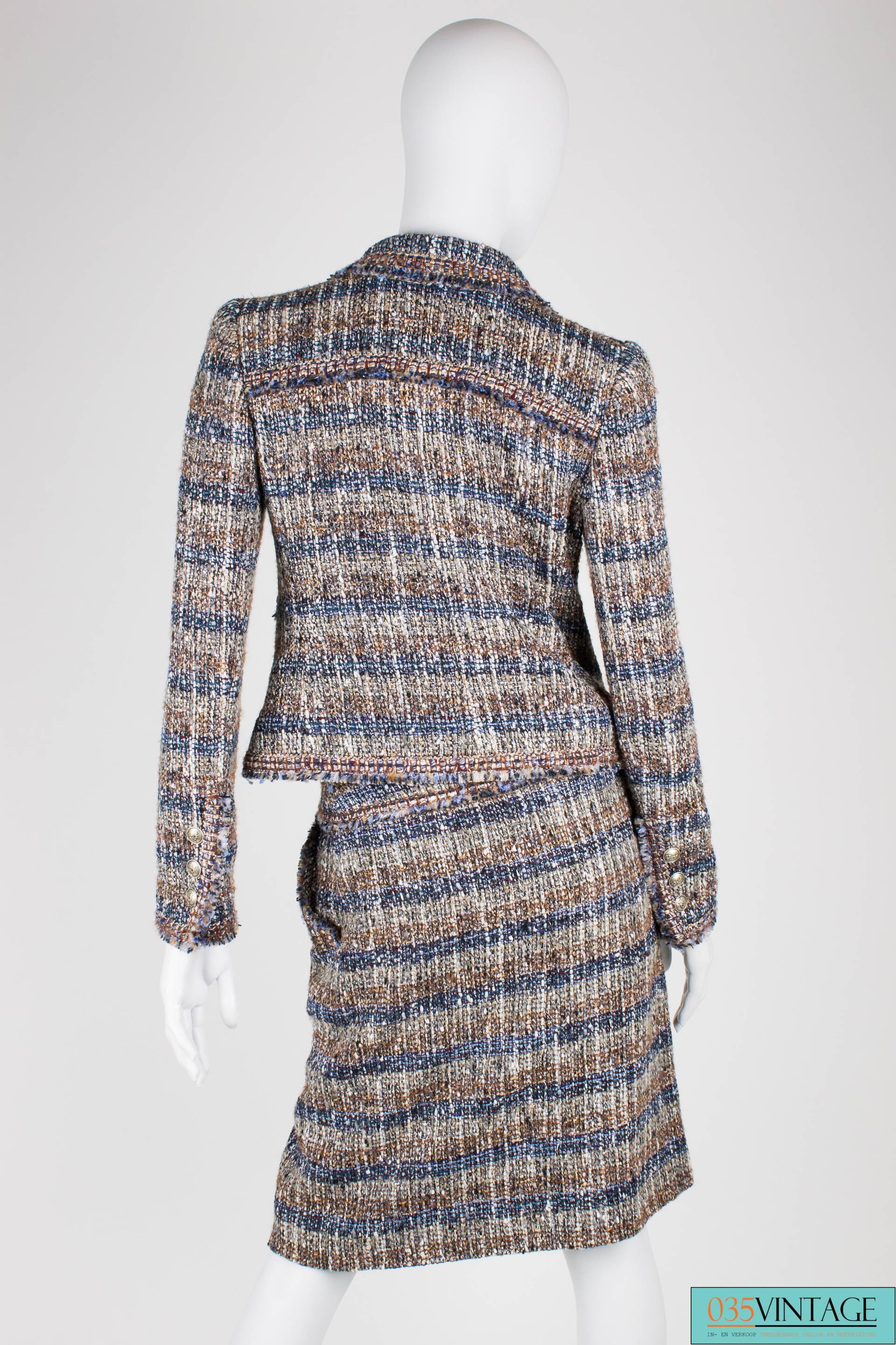 Absolutely gorgeous two-piece suit by Chanel in multi coloured boucle, mainly blue, brown, grey and silver.

The jacket has substantial lapels and front closure with two invisible hook-and-eyes. At the front four pockets in total, two above each