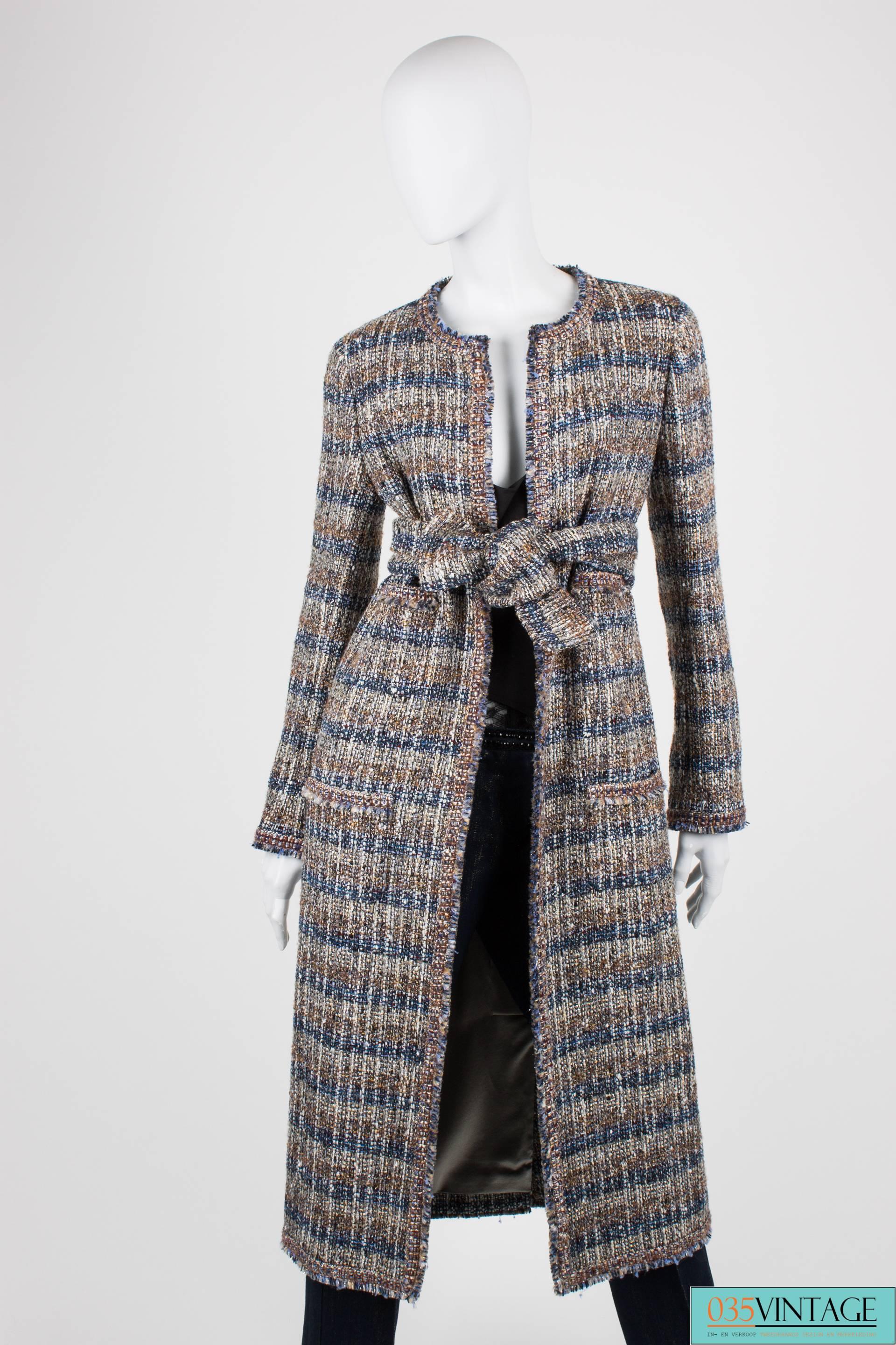 Gorgeous long coat by Chanel in multi coloured boucle, mainly blue, brown, grey and silver.

This mantle is collarless and has no closure at the front. Of course it can be closed with the matching belt. At the front four pockets in total; two on