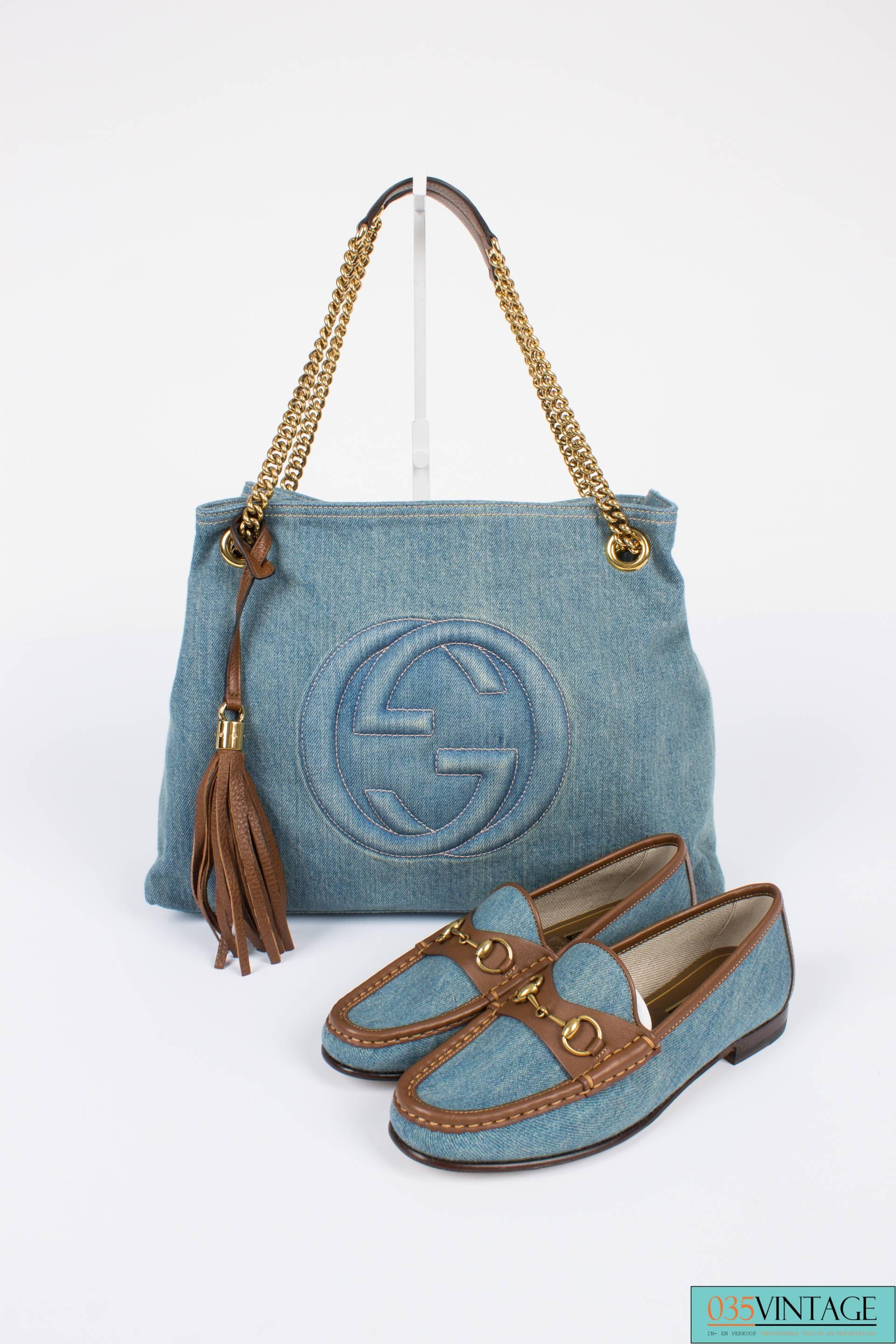A blue denim bag by Gucci with brown leather trim and gold-tone hardware, a careless beauty!

This Gucci Blue Denim Medium Soho Tote Bag is fully crafted in light blue denim, a frontal stitched interlocking GG logo and the interior is lined with