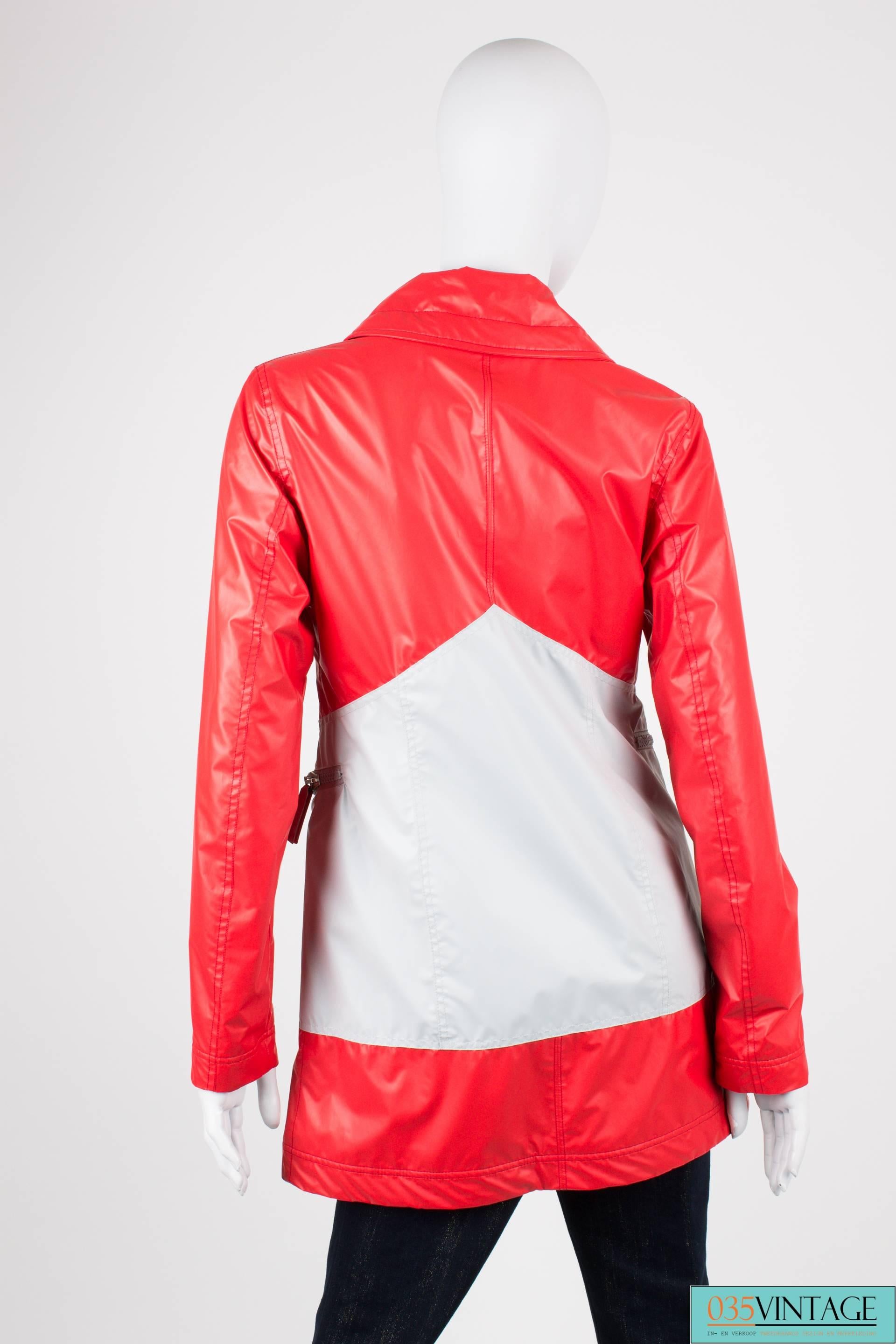 Sophisticated in the rain! A sporty raincoat by Chanel in red and grey. Cool!

This bright red parka has two large zip pockets at the front in the light grey area, this grey part goes all the way to the back. Two zippers at the chest. A large