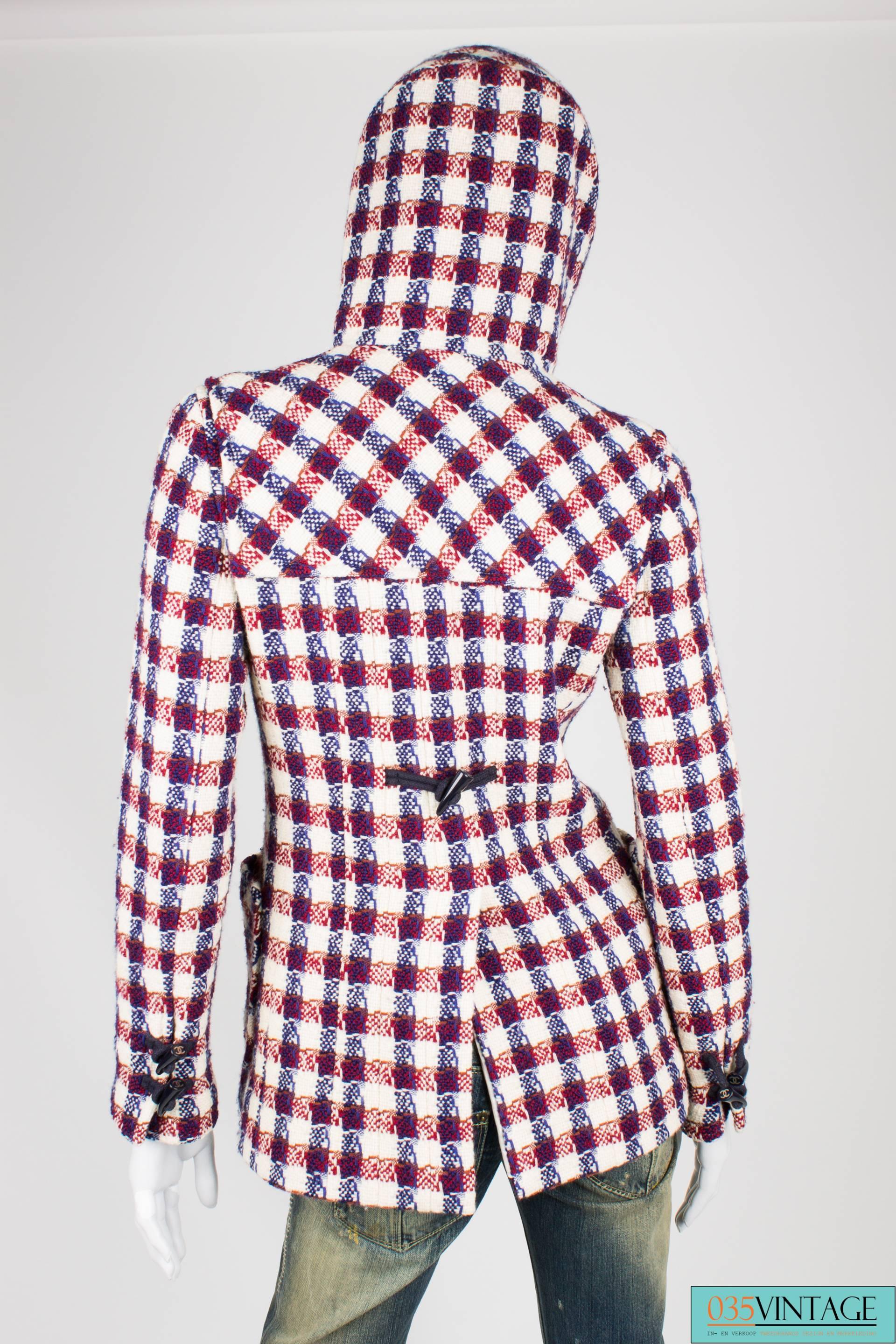 Red, white and blue checkered hooded jacket by Chanel. 

This woven jacket is made of 100% wool and has a toggle fastening at the front. These toggles are made of dark blue plastic and they hold a silver interlocking CC logo. At the end of the