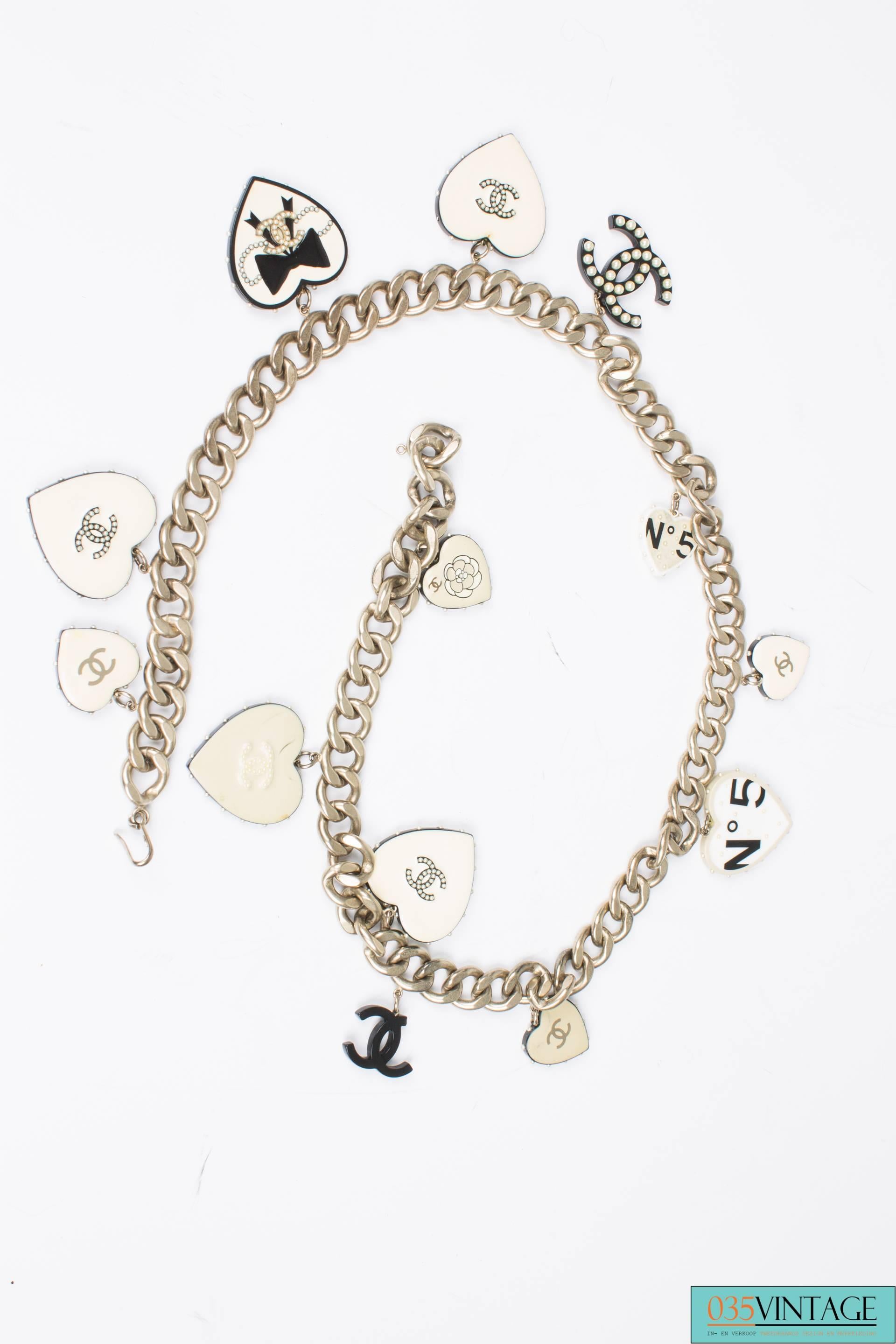 Matte silver Chanel chain waist belt that holds 11 black & white hearts in different sizes.

The chain measures 90 centimeters and closes with a little hook. The hearts all have different images and covered with little pearls. Two CC shaped