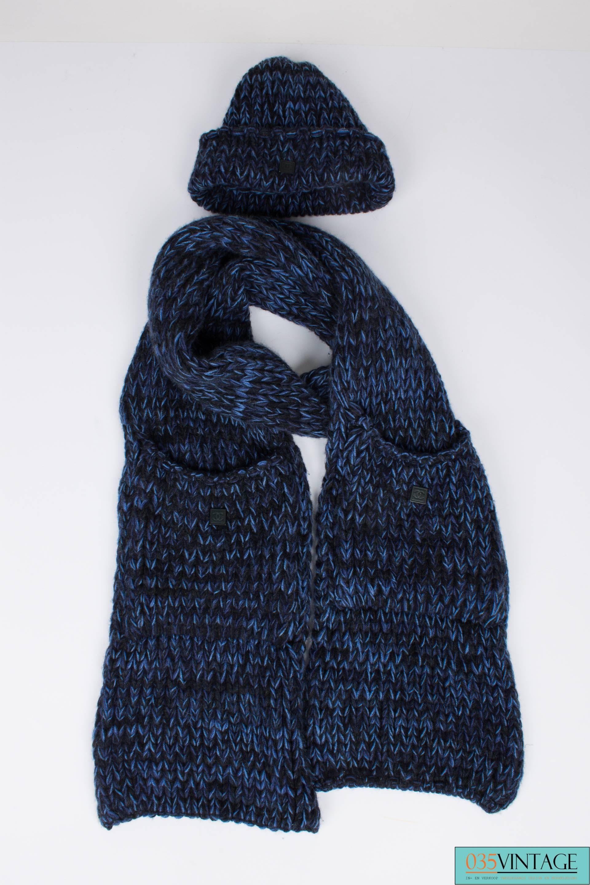 Two-piece Chanel set; a knitted hat and a scarf, both in a chunky crochet knit in black and blue cashmere. The hat has a round shape and a fold over where you will find a square black metal tag with CC-logo.

The scarf has an enormous length, it