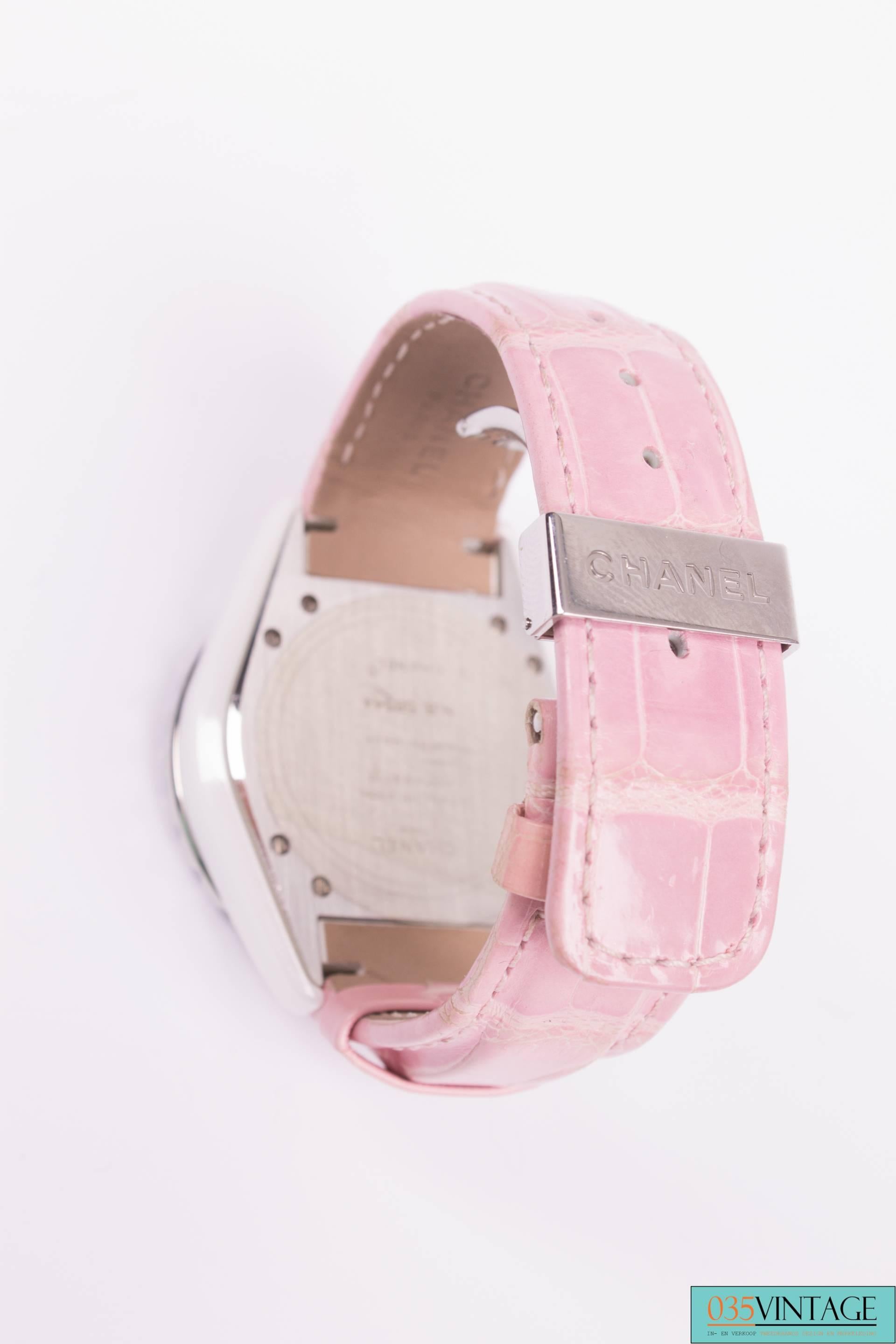 A watch made by Chanel with circular dial and pink sapphire set bezel, this is the J12.

The dial in white with black characters and date aperture. Ceramic and stainless steel case, the diameter is 4 centimeters. A pink alligator strap with silver