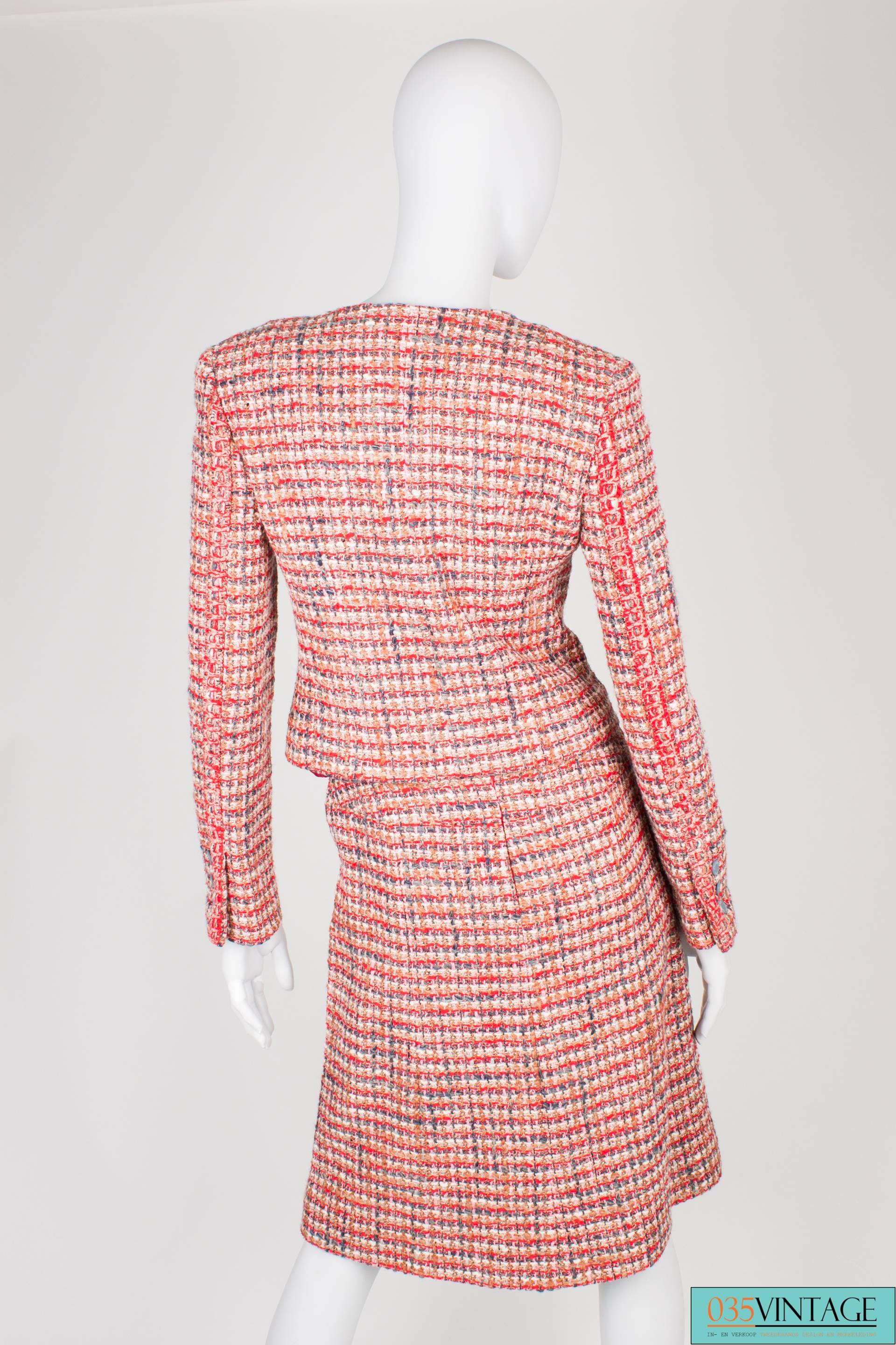 Stylish Chanel suit in a nice and warm color scheme; red, pink, gray,brown and white.

The short jacket has a rond collar and zip closure at the front. Two little patch pockets. At the end of the sleeves three gray buttons, stamped with the words
