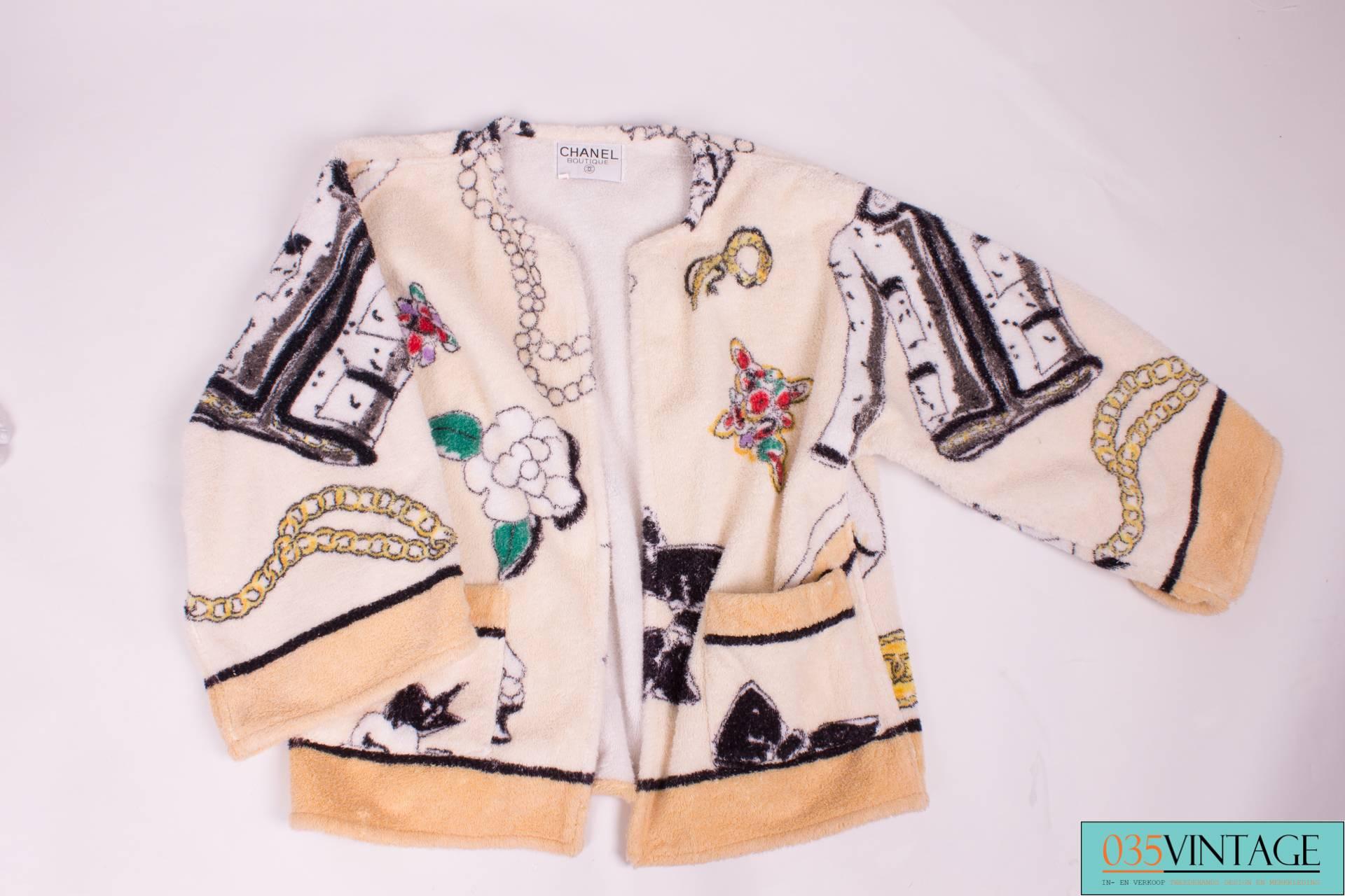 Lovely little bathrobe by Chanel from 1994; real vintage!

The white terry cloth jacket has an all-over print in black, yellow, red, purple, green, gray and beige with a hat, big bow, brooch, pumps, chains, bags and of course the famous camellia