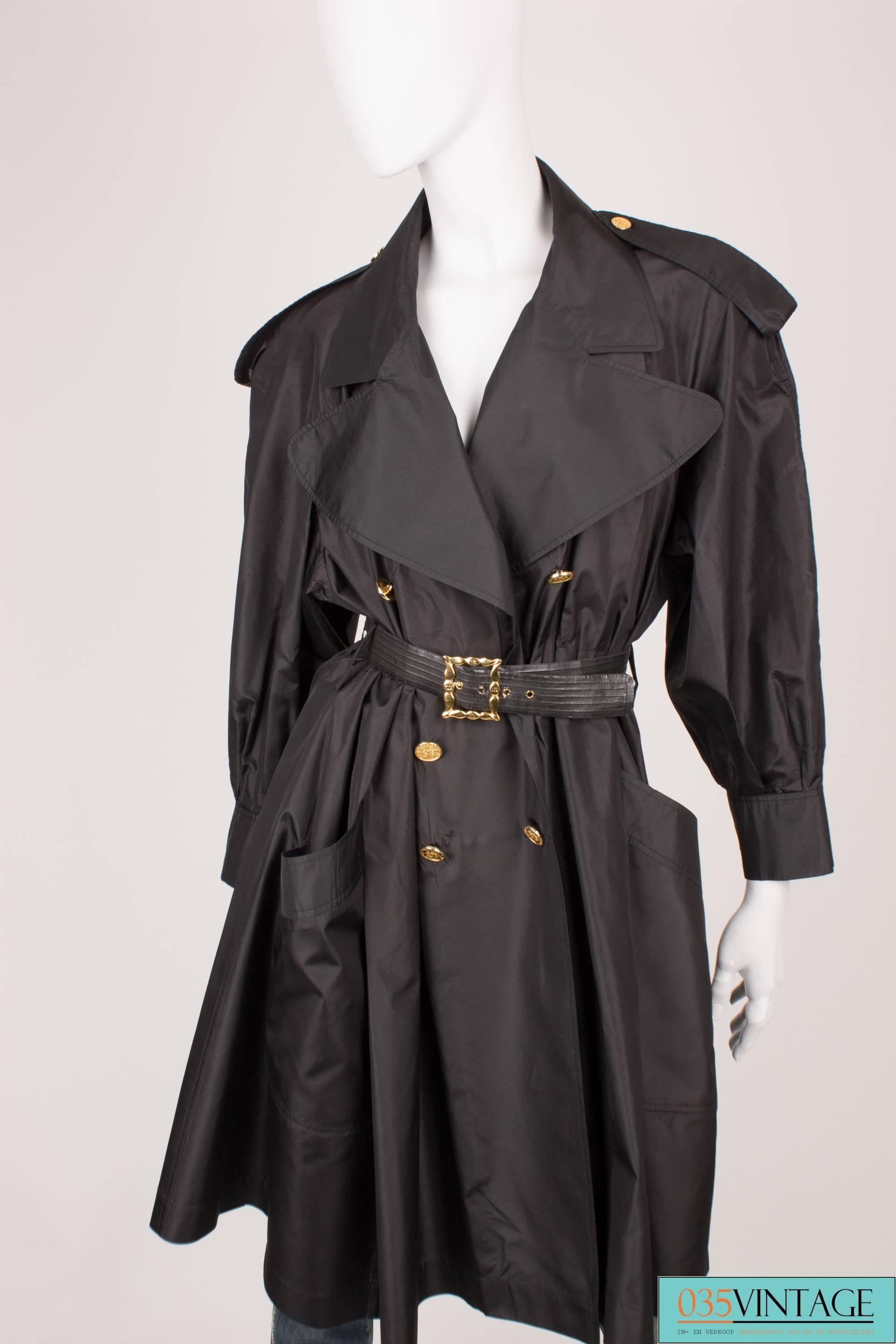 This vintage black nylon trenchcoat by Chanel is a real masterpiece.

It is from the ready-to-wear spring/summer collection of 1988, has 7/8 sleeves with a wide brim at the end, six large golden buttons at the front, a rather large collar, extra