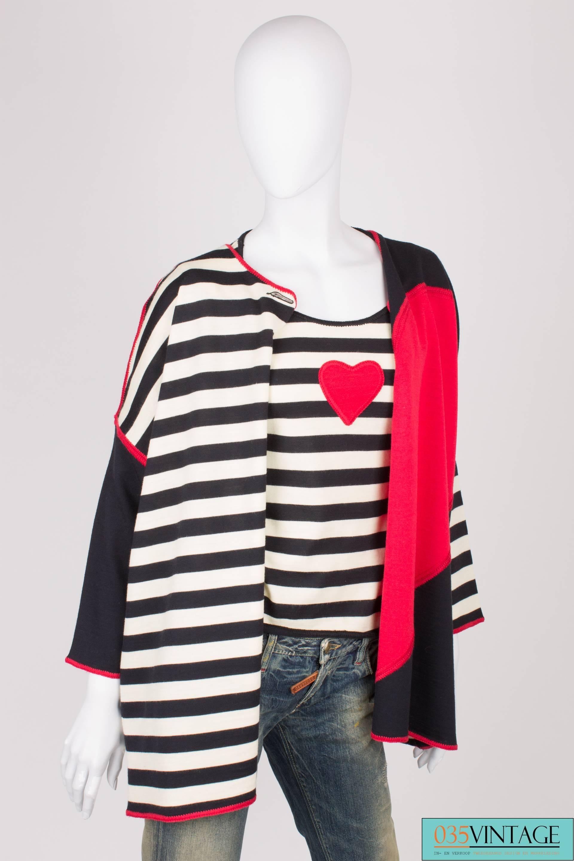 A warm vintage cardigan by Moschino Cheap and Chic in red, white and black wool.

The cardigan has one button closure, just below the neckline. One of the panels is striped in black and white, the other one is black with half a heart in red. On