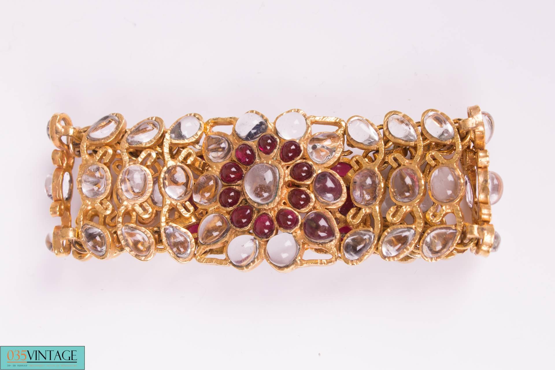 This beautiful vintage bracelet by Chanel is covered with rhinestones in different shapes and sizes and have a blue/grayish glow.

In the center and at the ends you will find the same rhinestones in coral red. Hook-and-eye closure, length of the