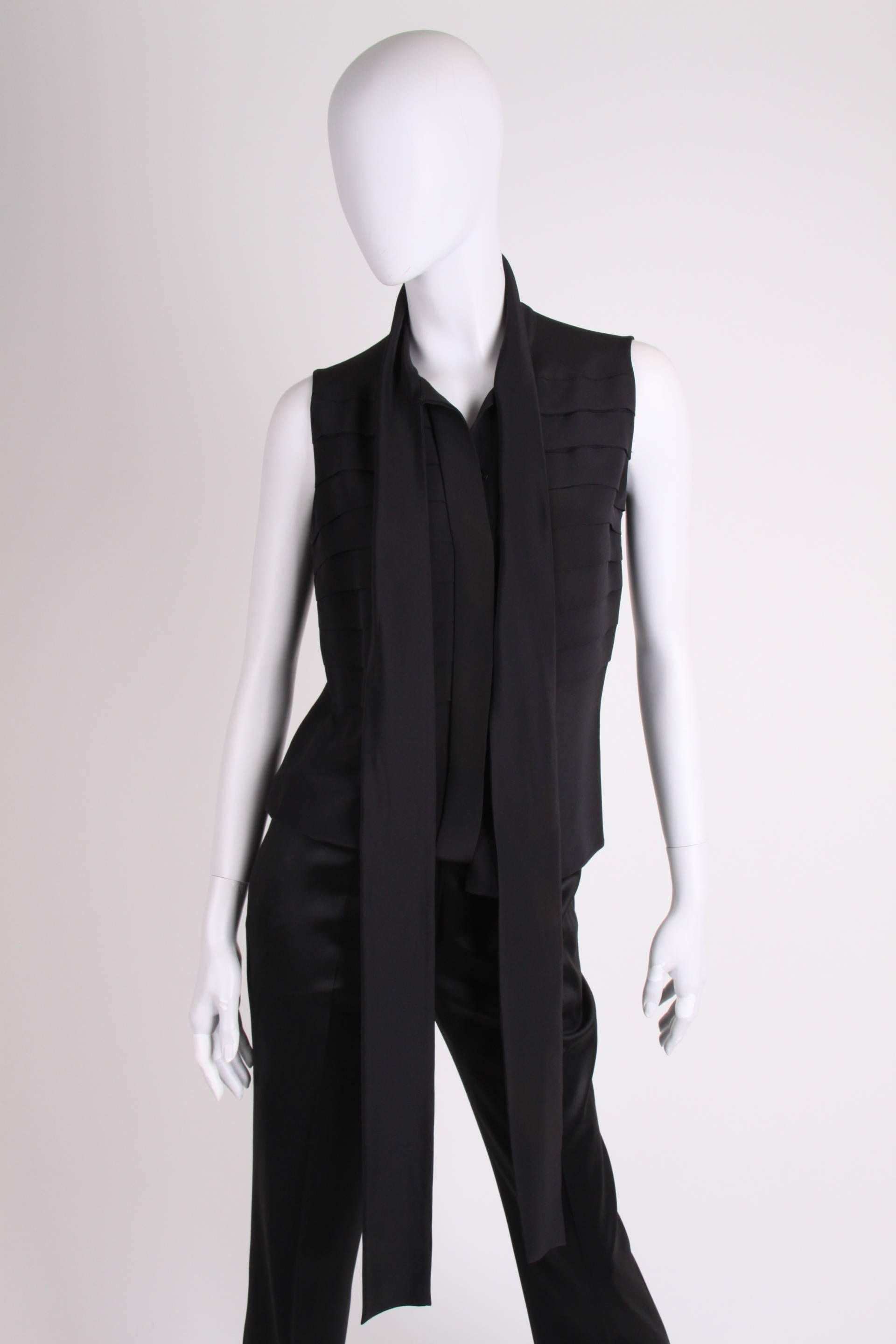 Elegant sleeveless blouse by Chanel in black silk, an oldtime classic!

This blouse has hip length and button closure up front. Eight stitched horizontal pleats in the upper part on the front and back. The collar is a rather long and wide ribbon of