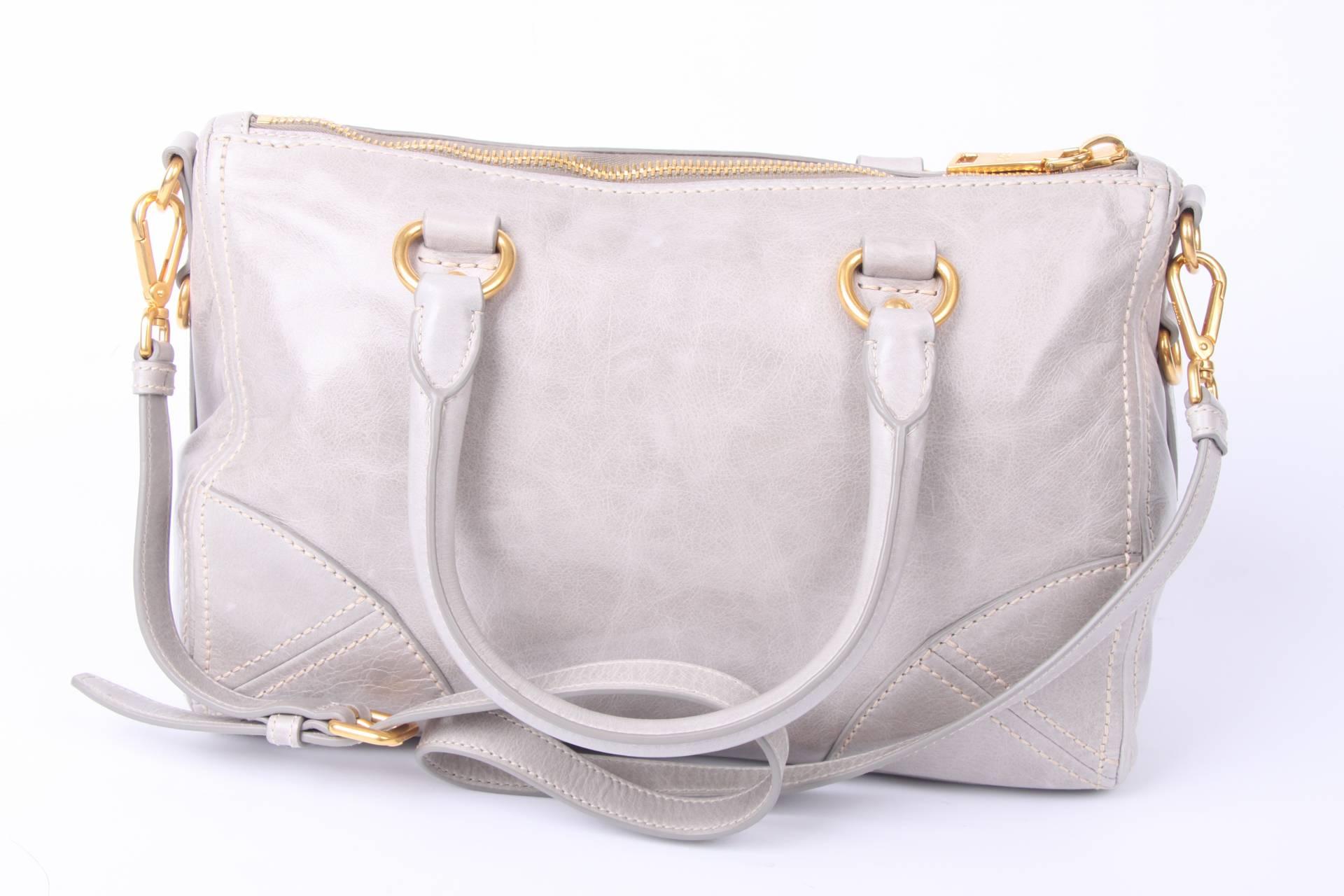 Prada bag crafted in light gray leather in a super handy big size.

This bag has short handles and also a long (adjustable and detachable) shoulder strap. Gold-tone hardware, a PRADA logo at the front and a zipper underneath.

Zip top closure and
