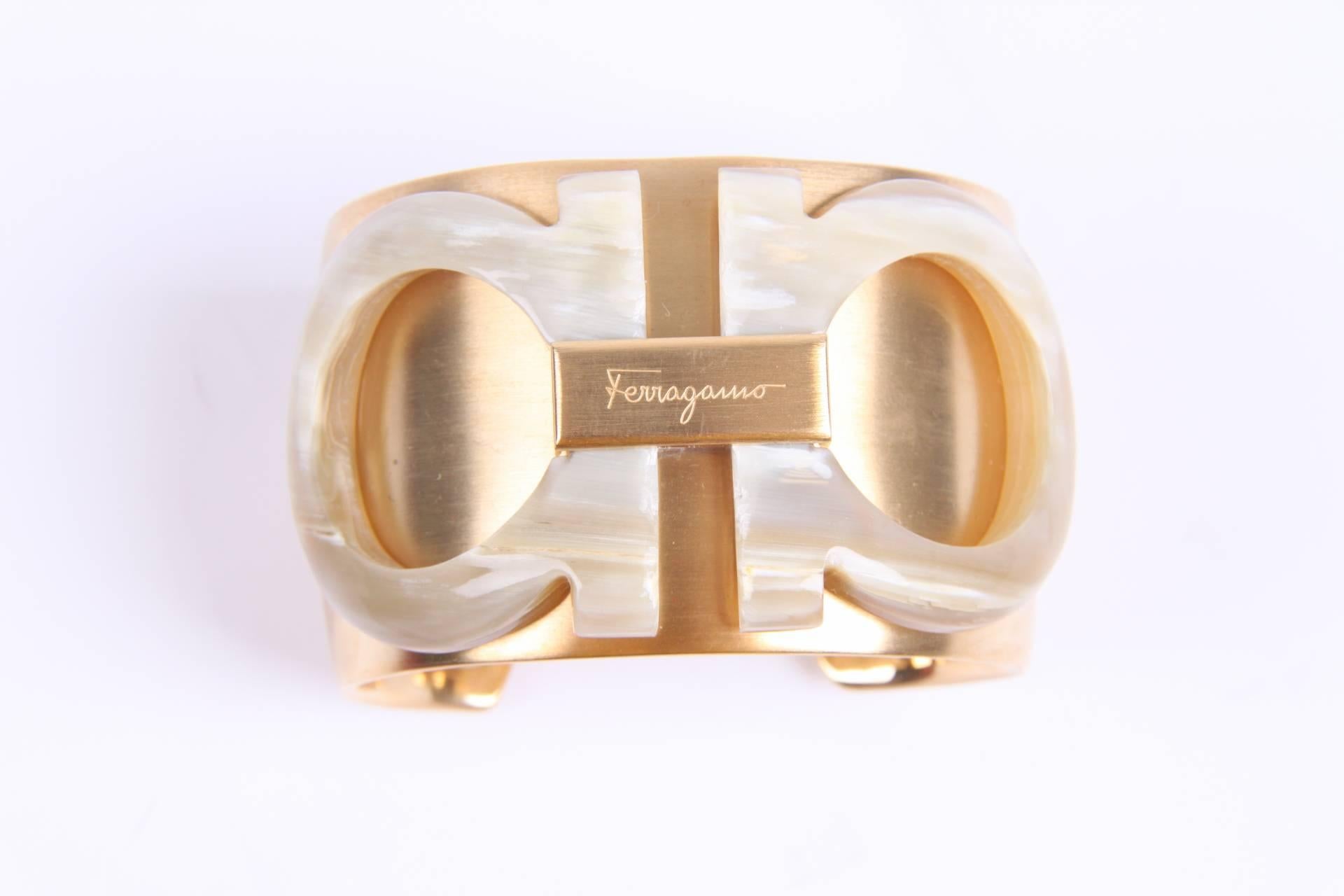 Super cool cuff bracelet by Salvatore Ferragamo, the bone logo that is place on top is called Gancini.

Crafted in heavy metal with a matte gold-tone finish. And,... we have two of these beauties! Fantastic to wear them both on the same time, one on