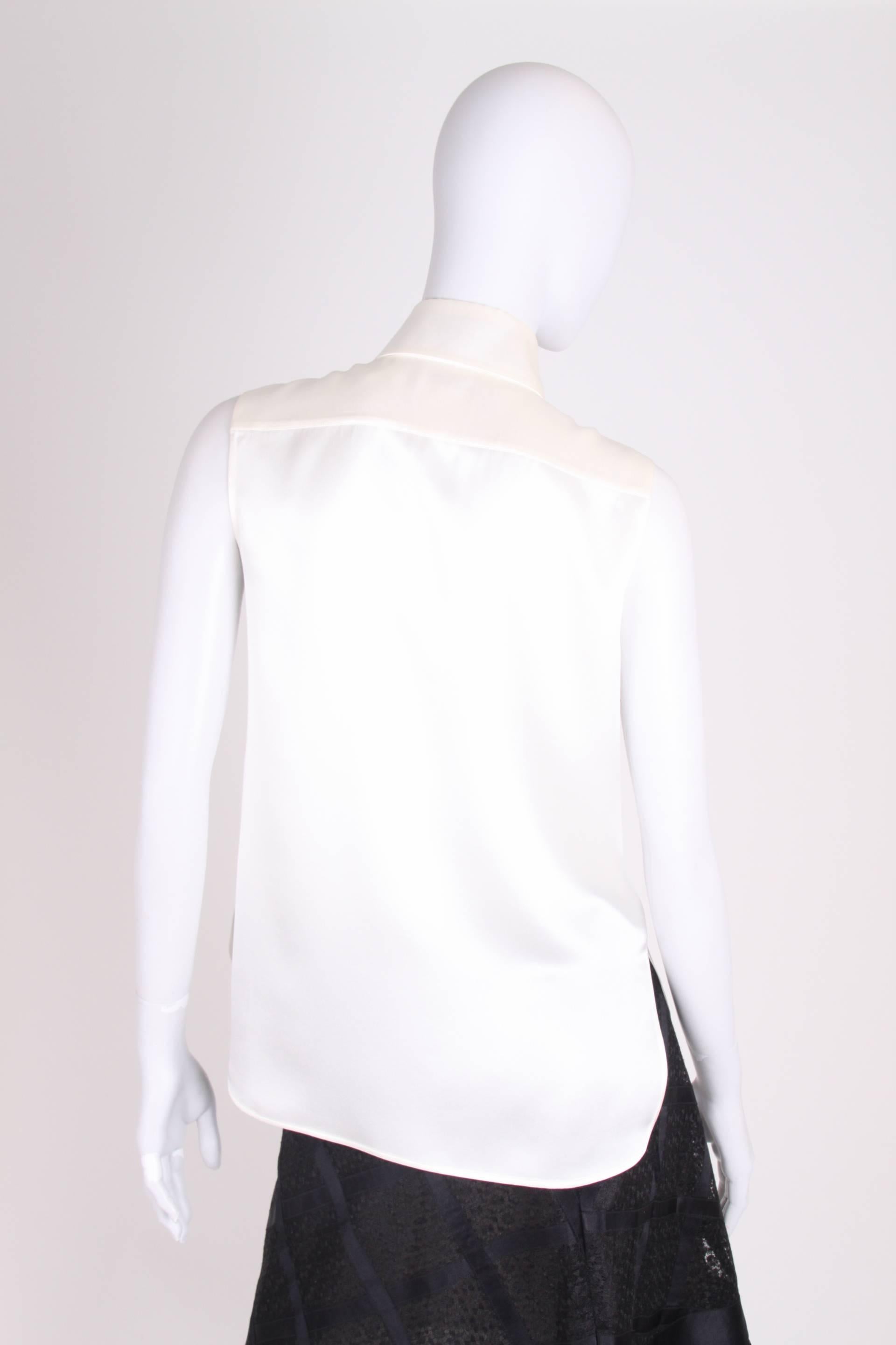 Elegant sleeveless blouse by Chanel, very presentable!

This blouse has button closure at the front; five white buttons with a CC-logo. Two large patch pockets on the chest and a rather large collar with a wide black ribbon that can be tied into a