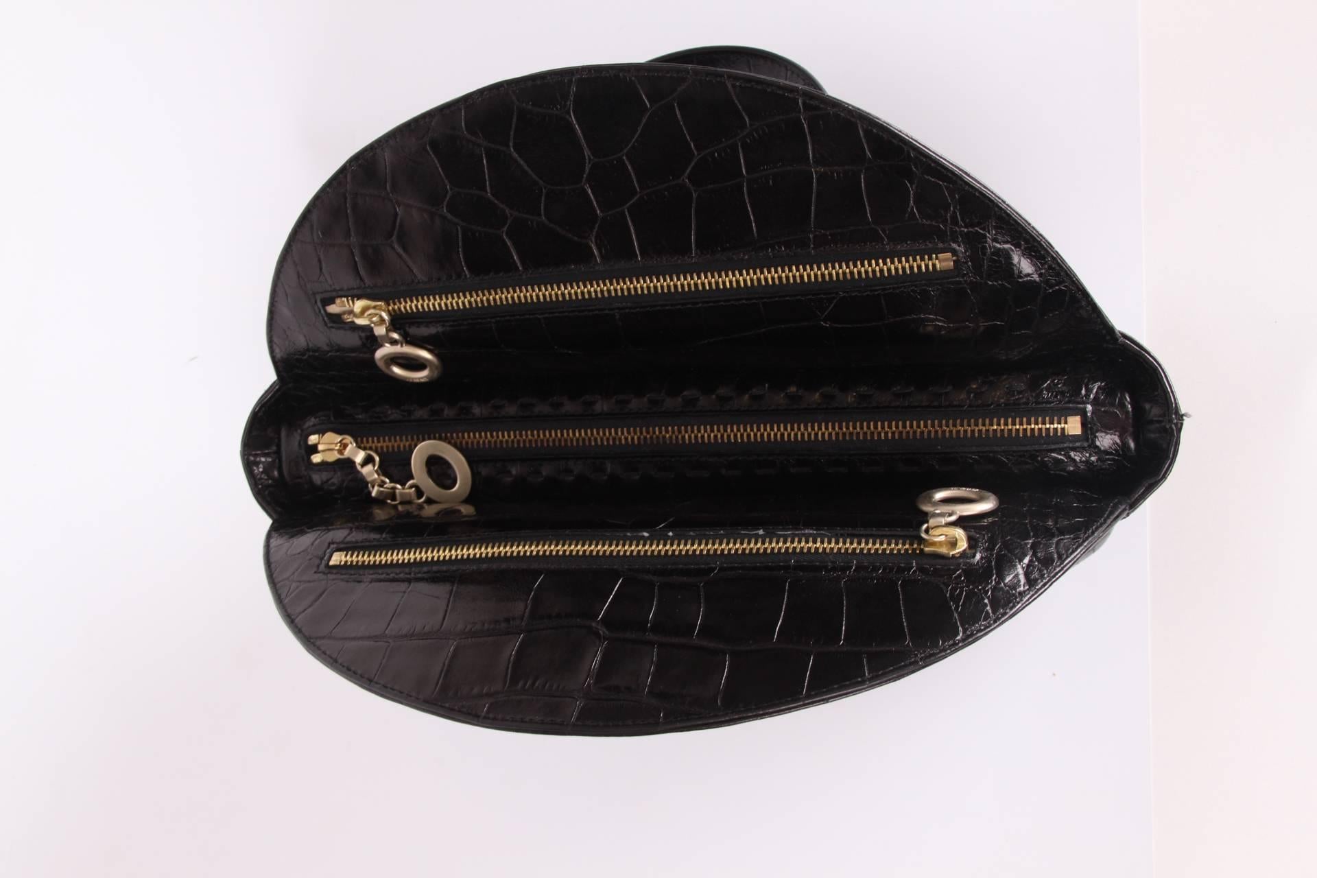 Stylish bag in black leather covered with a croco print by Versace.

This round bag has a compartment with flap and push button on the front and back. Two handles on top, zip closure. Matte gold-tone hardware.

Interior lining in nude coloured