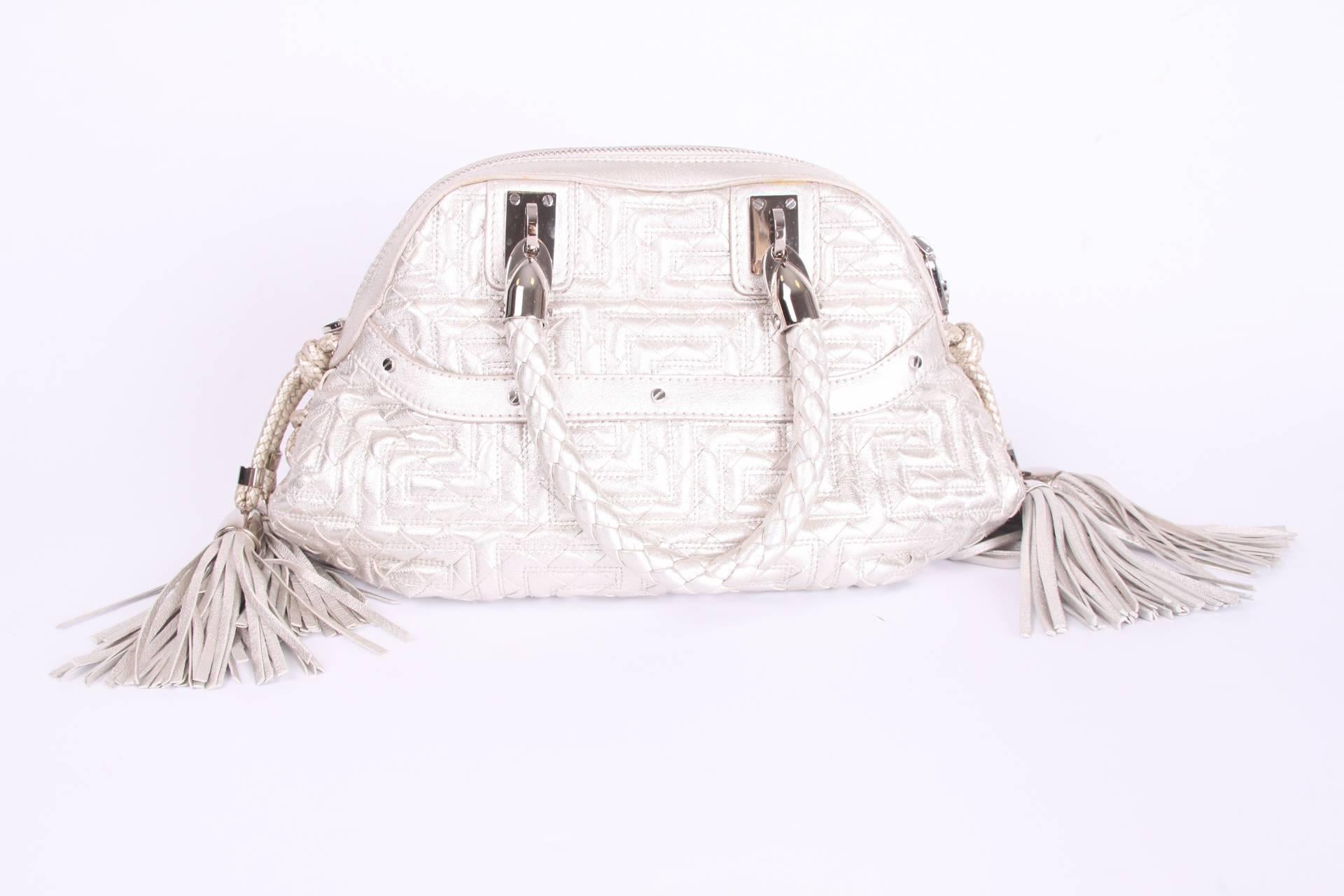 Wonderful top-handle bag by Gianni Versace Couture crafted in metallic silver-tone leather.

Two braided handles on top, zip top closure. On both sides of the bag two large braided leather tassels and a front pocket with a zipper. A shiny