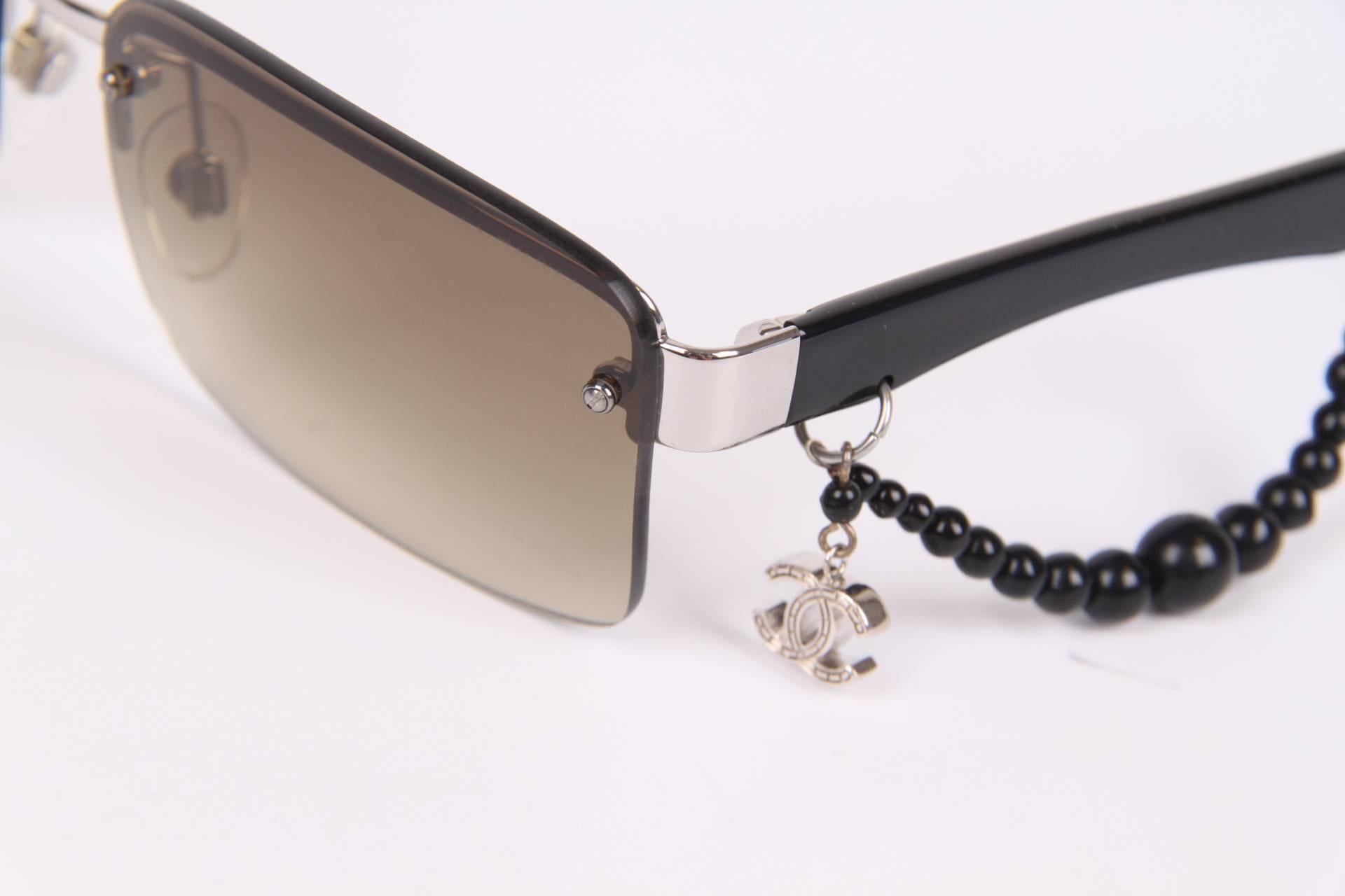 Charming pair of Chanel sunglasses with a silver-tone CC charm and a black string of beads on one of the temples.

The lenses are in a dégradé brown colour, the temples are crafted in black acetate and silver-tone accents. Different sizes of black