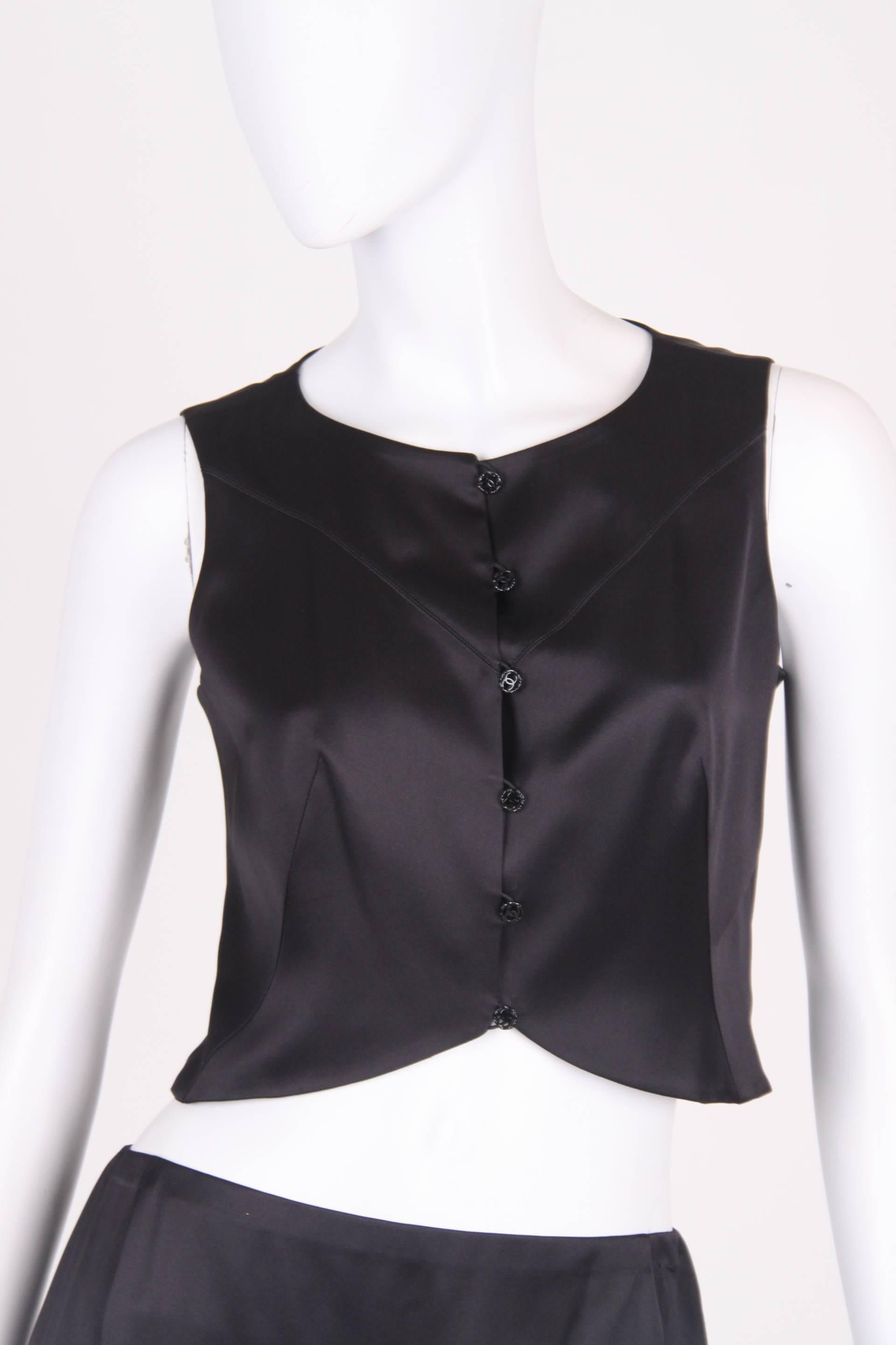 Stylish two piece suit by Chanel; a black silk top and skirt.

The sleeveless top has tailored fitting and front closure with six metal buttons. These shiny black buttons all have a CC logo in the center. A round neckline and fully lined.

Size: